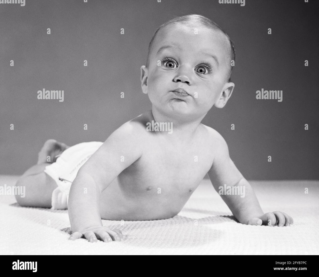 1960s BABY LYING ON STOMACH FUNNY FACIAL EXPRESSION BIG EYES AND PURSED  LIPSLLOKING AT CAMERA - b22299 HAR001 HARS B&W WIDE BUG-EYED HUMOROUS  STOMACH COMICAL PURSED DIAPERS ANIMATED COMEDY BABY BOY WIDE-EYED