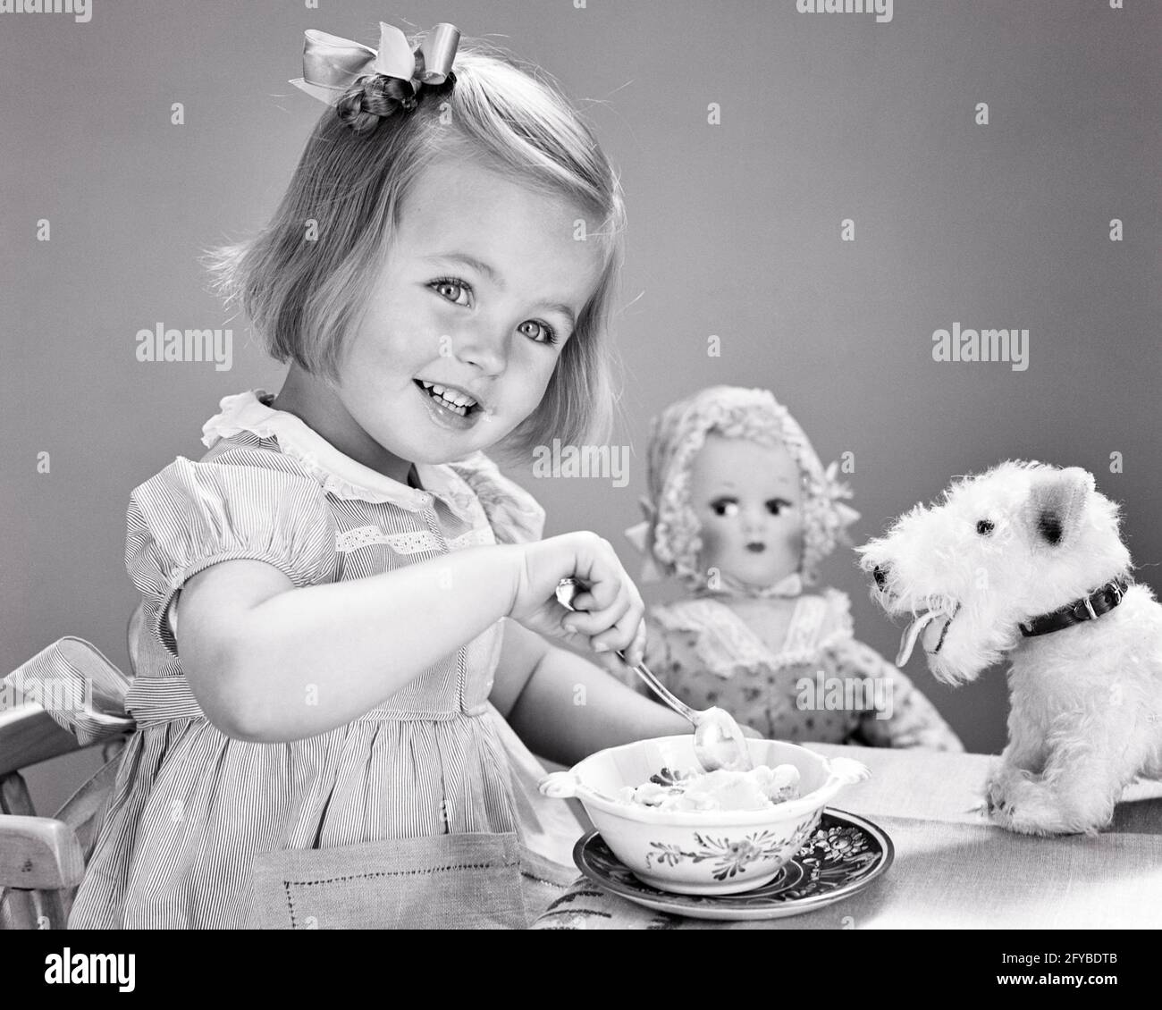1940s 1950s SMILING GIRL BOW IN HAIR EATING BOWL OF ICE CREAM LOOKING AT CAMERA SURROUNDED BY STUFFED ANIMAL DOG AND DOLL TOYS  - f2693 HAR001 HARS JOY LIFESTYLE FEMALES WINNING STUDIO SHOT STUFFED HEALTHINESS HOME LIFE COPY SPACE HALF-LENGTH B&W HUMOROUS HAPPINESS CHEERFUL AND NUTRITION SURROUNDED COMICAL BY SMILES COMEDY CONSUME CONSUMING JOYFUL NOURISHMENT STYLISH ICE CREAM PLEASANT AGREEABLE CHARMING GROWTH JUVENILES LOVABLE PLEASING ADORABLE APPEALING BLACK AND WHITE CAUCASIAN ETHNICITY HAR001 OLD FASHIONED Stock Photo