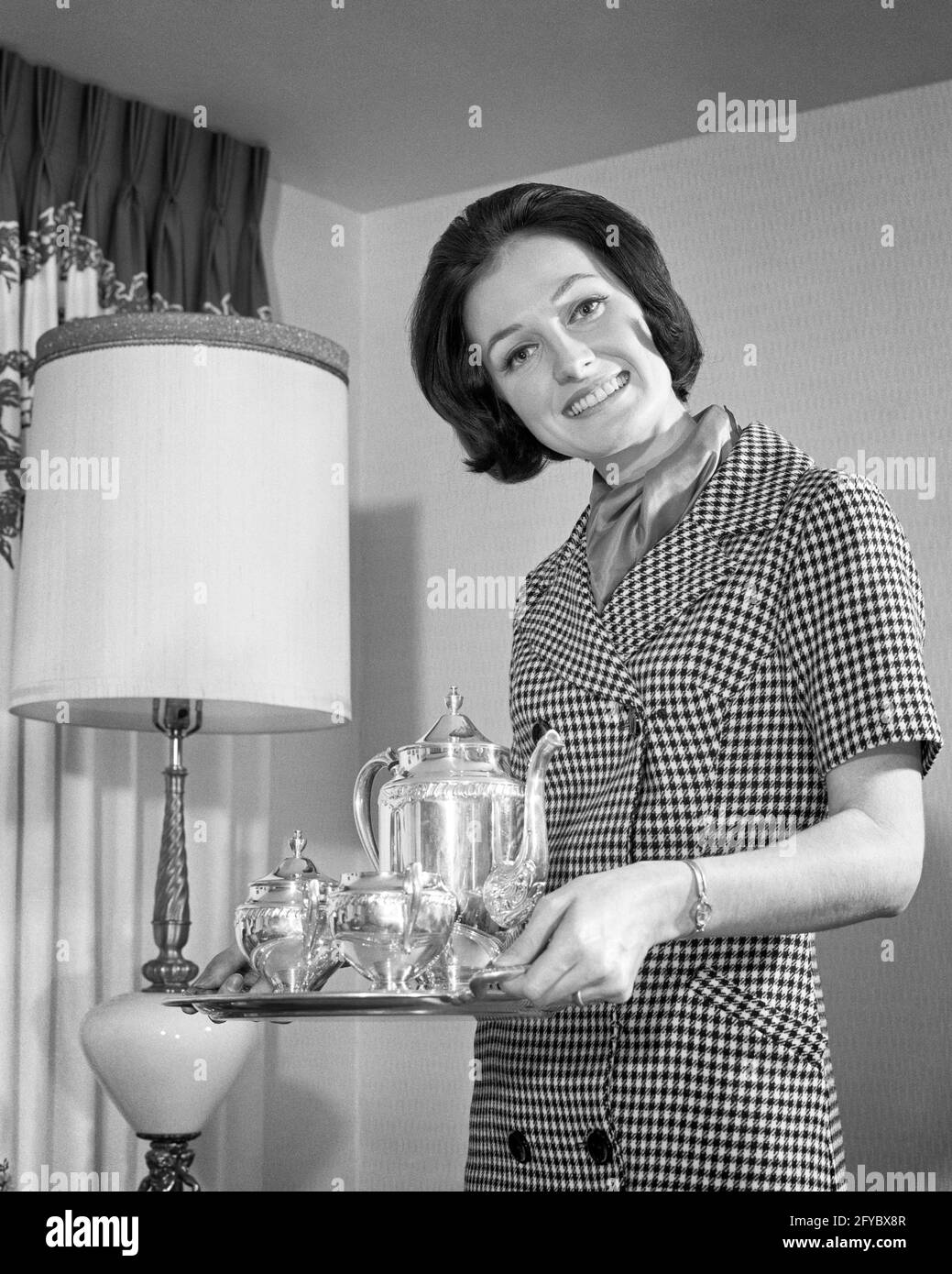 1960s SMILING DARK HAIRED WOMAN HOSTESS LOOKING AT CAMERA CARRYING SILVER COFFEE SERVICE AT HOME NODDING HER HEAD IN WELCOME - h7342 HAR001 HARS FACIAL WELCOME YOUNG ADULT PLEASED ENTERTAINING JOY LIFESTYLE FEMALES HOME LIFE COPY SPACE HALF-LENGTH LADIES PERSONS CARING CONFIDENCE EXPRESSIONS B&W EYE CONTACT BRUNETTE HOMEMAKER HAPPINESS HOMEMAKERS CHEERFUL LEISURE LOW ANGLE RECREATION HOSTESS PRIDE AT IN GUESTS HOUSEWIVES SMILES HOST STERLING CONCEPTUAL JOYFUL STYLISH SUPPORT CREAMER NODDING RELAXATION U YOUNG ADULT WOMAN BLACK AND WHITE CAUCASIAN ETHNICITY GUEST HAR001 OLD FASHIONED Stock Photo