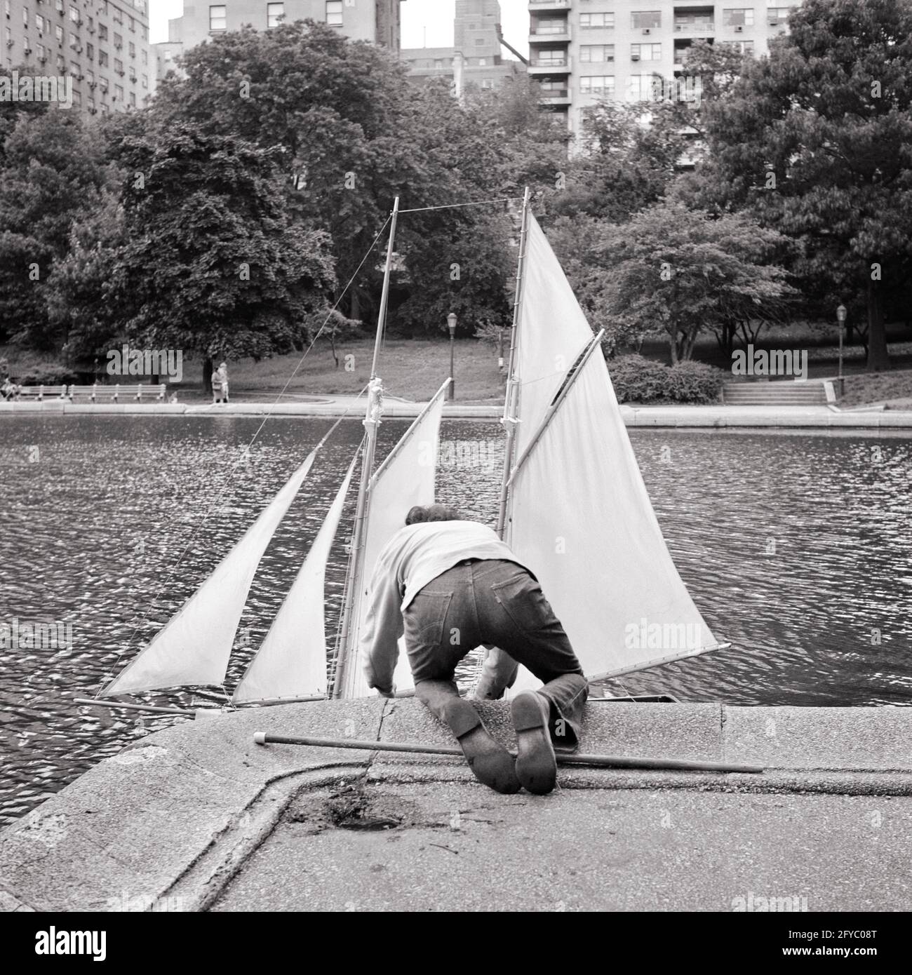 1970s REAR VIEW ANONYMOUS BOY PUTTING TOY SAILBOAT INTO CONSERVATORY POND CENTRAL PARK NEW YORK CITY USA - j13421 HAR001 HARS SKILL ACTIVITY AMUSEMENT ADVENTURE HOBBY INTEREST EXCITEMENT HOBBIES KNOWLEDGE RECREATION PASTIME PLEASURE REAR VIEW NYC FROM BEHIND NEW YORK CITIES IMAGINATION CONSERVATORY NEW YORK CITY ANONYMOUS BACK VIEW JUVENILES PRE-TEEN PRE-TEEN BOY RELAXATION AMATEUR BLACK AND WHITE CAUCASIAN ETHNICITY CENTRAL PARK ENJOYMENT HAR001 OLD FASHIONED Stock Photo