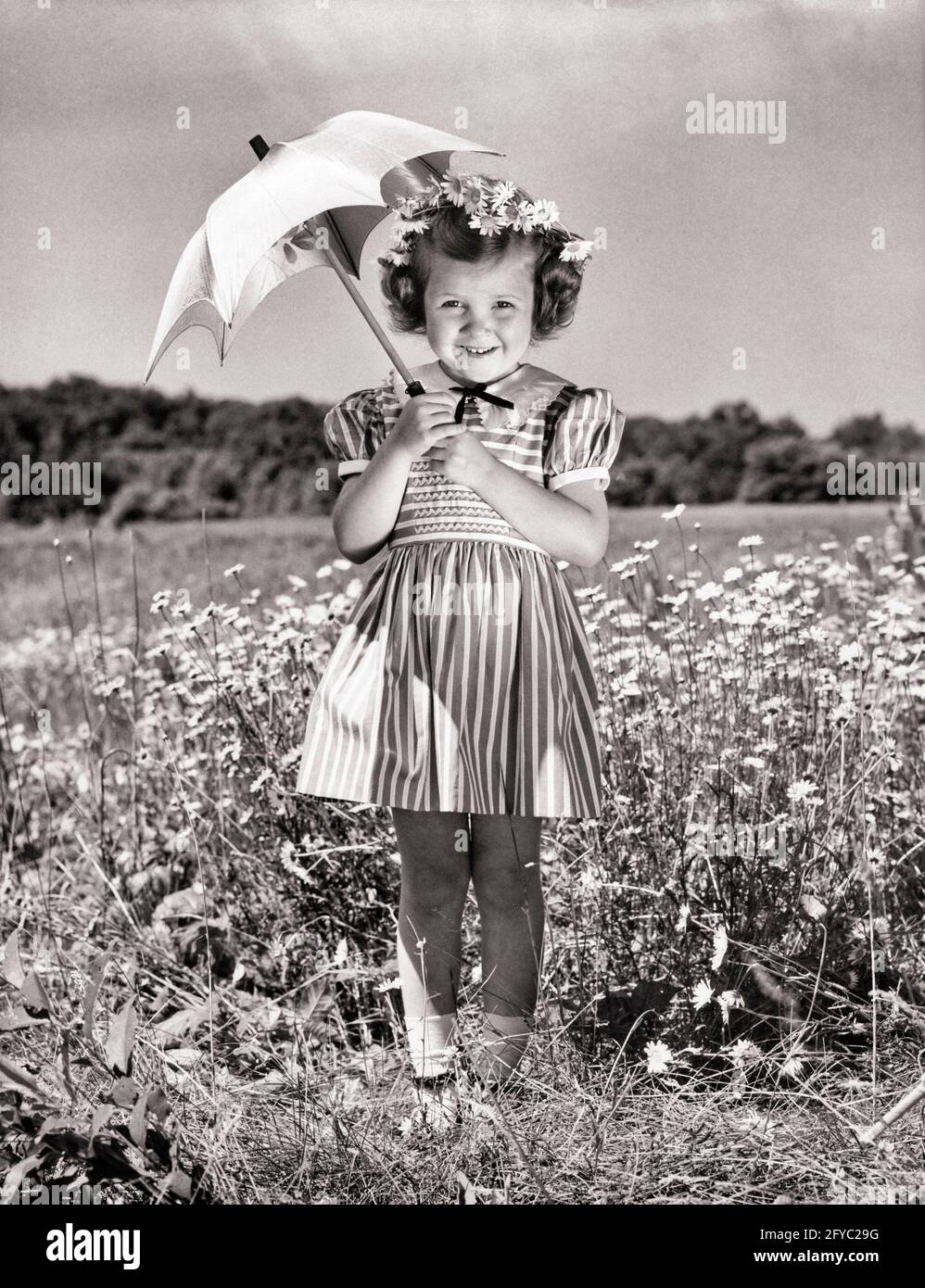 1940s 1950s SMILING GIRL UNDER PARASOL STANDING IN FIELD OF DAISIES WEARING  STRIPED DRESS FLOWERS IN HER HAIR LOOKING AT CAMERA - j1894 HAR001 HARS JOY  LIFESTYLE SATISFACTION FEMALES STRIPED RURAL HEALTHINESS