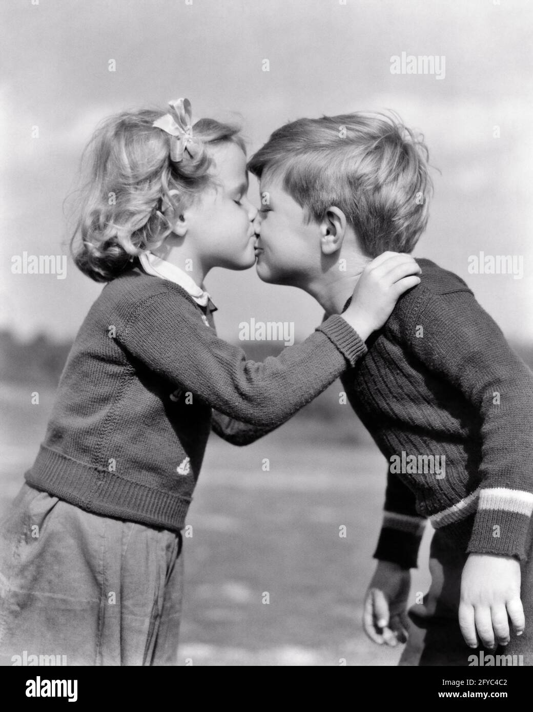 1930s 1940s SERIOUS LITTLE GIRL KISSING SMILING LITTLE BOY BOTH OUTDOORS WEARING KNIT WOOL SWEATERS - j8696 HAR001 HARS HEALTHINESS HOME LIFE WOOL COPY SPACE FRIENDSHIP HALF-LENGTH CARING MALES B&W KNIT HAPPINESS SWEATERS CONNECTION CONCEPTUAL FRIENDLY PERSONAL ATTACHMENT PLEASANT PUPPY LOVE AFFECTION AGREEABLE CHARMING EMOTION JUVENILES LOVABLE PECK PLEASING SMOOCH TOGETHERNESS ADORABLE APPEALING BLACK AND WHITE CAUCASIAN ETHNICITY HAR001 OLD FASHIONED Stock Photo