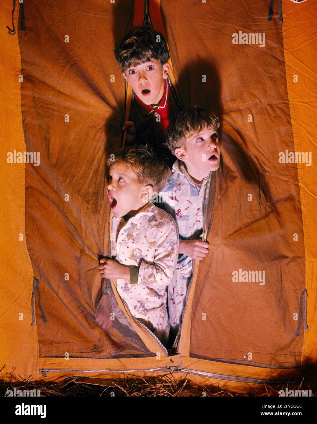 1960s CAMPING ADVENTURE THREE SCARED FRIGHTENED BOYS BROTHERS LOOKING OUT OF TENT FLAP OPENING AT NIGHT ONE LOOKING AT CAMERA  - kc3906 CRS001 HARS LIFESTYLE BROTHERS RURAL HEALTHINESS COPY SPACE FRIENDSHIP HALF-LENGTH MALES FRIGHTENED SIBLINGS WIDE EYE CONTACT BUG-EYED HEAD AND SHOULDERS ADVENTURE EXCITEMENT RECREATION AWAKE SIBLING TERRIFIED CONCEPTUAL IMAGINATION WIDE-EYED GROWTH JUVENILES STARTLED TOGETHERNESS ALARMED CAUCASIAN ETHNICITY OLD FASHIONED Stock Photo