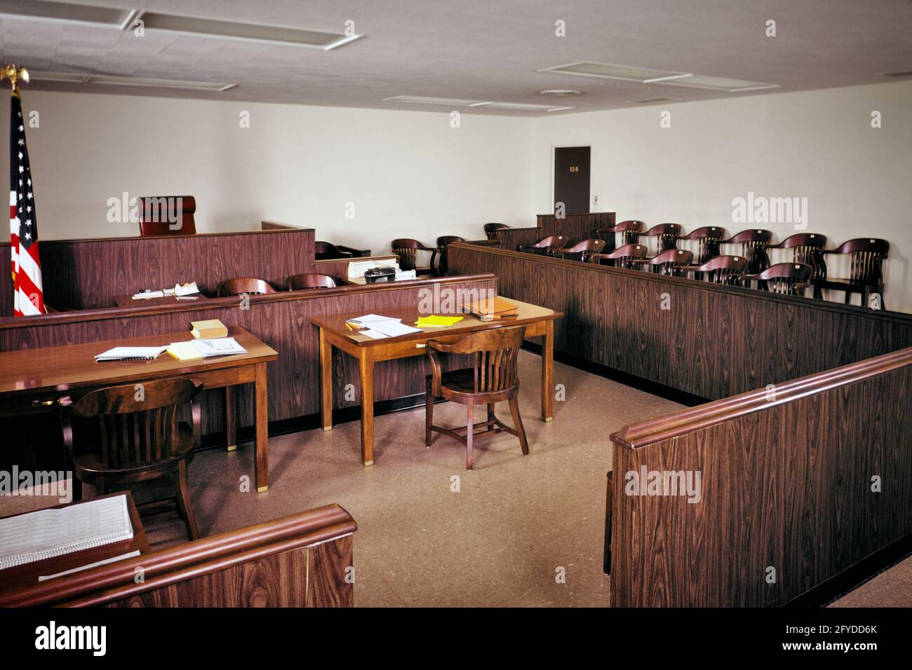 1970s INTERIOR OF EMPTY PUBLIC USA COURTROOM WITH JUDGE’S BENCH JURY BOX DEFENSE AND PROSECUTION TABLES AMERICAN FLAG  - ki4960 HAR001 HARS NORTH AMERICAN LOCATION AND POWERFUL RAILING COURTHOUSE OF AUTHORITY OCCUPATIONS POLITICS CONCEPTUAL PLAIN PROSECUTION JURY BOX COOPERATION DEFENSE FUNCTIONAL PLAINTIFF TYPICAL 12 AMERICAN FLAG HAR001 OLD FASHIONED Stock Photo