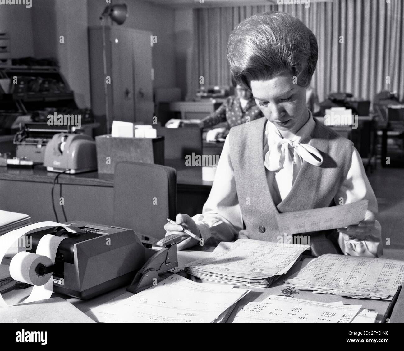 1960s OFFICE WORKER WOMAN WITH TEASED BIG HAIR HAIRSTYLE WORKING AT DESK WITH ADDING MACHINE AND HUGE PILES OF PAPERS - o2399 HAR001 HARS COPY SPACE HALF-LENGTH LADIES PERSONS PROFESSION B&W BEEHIVE SKILL OCCUPATION OFFICES SKILLS ADDING AND CAREERS HAIRSTYLE BOOKKEEPER LABOR OFFICE WORKER AT EMPLOYMENT OCCUPATIONS GAL FRIDAY ADMINISTRATOR SECRETARIES STYLISH EMPLOYEE AMANUENSIS INTENSE MID-ADULT MID-ADULT WOMAN SOLUTIONS TEASED BLACK AND WHITE BOUFFANT CAUCASIAN ETHNICITY CLERICAL HAR001 LABORING OLD FASHIONED Stock Photo