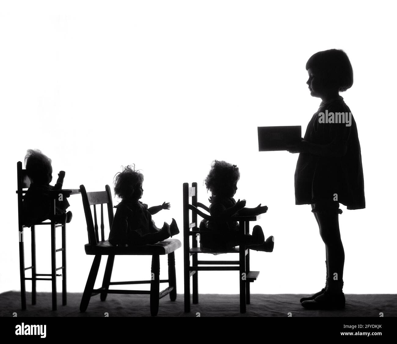 1920s SILHOUETTE OF LITTLE GIRL TEACHING READING TO DOLLS SITTING IN CHAIRS - s1782 HAR001 HARS SILHOUETTES B&W OUTLINE DREAMS HAPPINESS SILHOUETTED KNOWLEDGE LEADERSHIP OCCUPATIONS CONNECTION CONCEPTUAL IMAGINATION STYLISH ANONYMOUS GROWTH JUVENILES BLACK AND WHITE HAR001 OLD FASHIONED Stock Photo