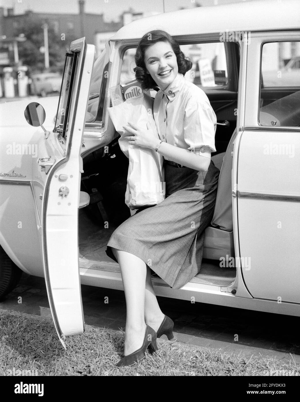 1950s SMILING BRUNETTE WOMAN GETTING OUT OF A CAR LOOKING AT CAMERA HOLDING A BAG OF GROCERIES - s6333 HAR001 HARS PLEASED JOY LIFESTYLE SATISFACTION FEMALES HEALTHINESS HOME LIFE COPY SPACE FULL-LENGTH LADIES PERSONS AUTOMOBILE CONFIDENCE TRANSPORTATION B&W SHOPPER EYE CONTACT BRUNETTE HOMEMAKER SHOPPERS HAPPINESS HOMEMAKERS CHEERFUL AUTOS PRIDE HOUSEWIVES SMILES CONCEPTUAL AUTOMOBILES JOYFUL STYLISH VEHICLES YOUNG ADULT WOMAN BLACK AND WHITE CAUCASIAN ETHNICITY HAR001 OLD FASHIONED Stock Photo