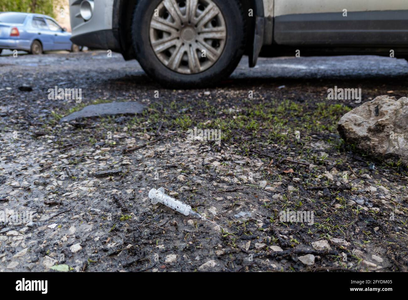 a used disposable syringe is lying on the ground near the car Stock