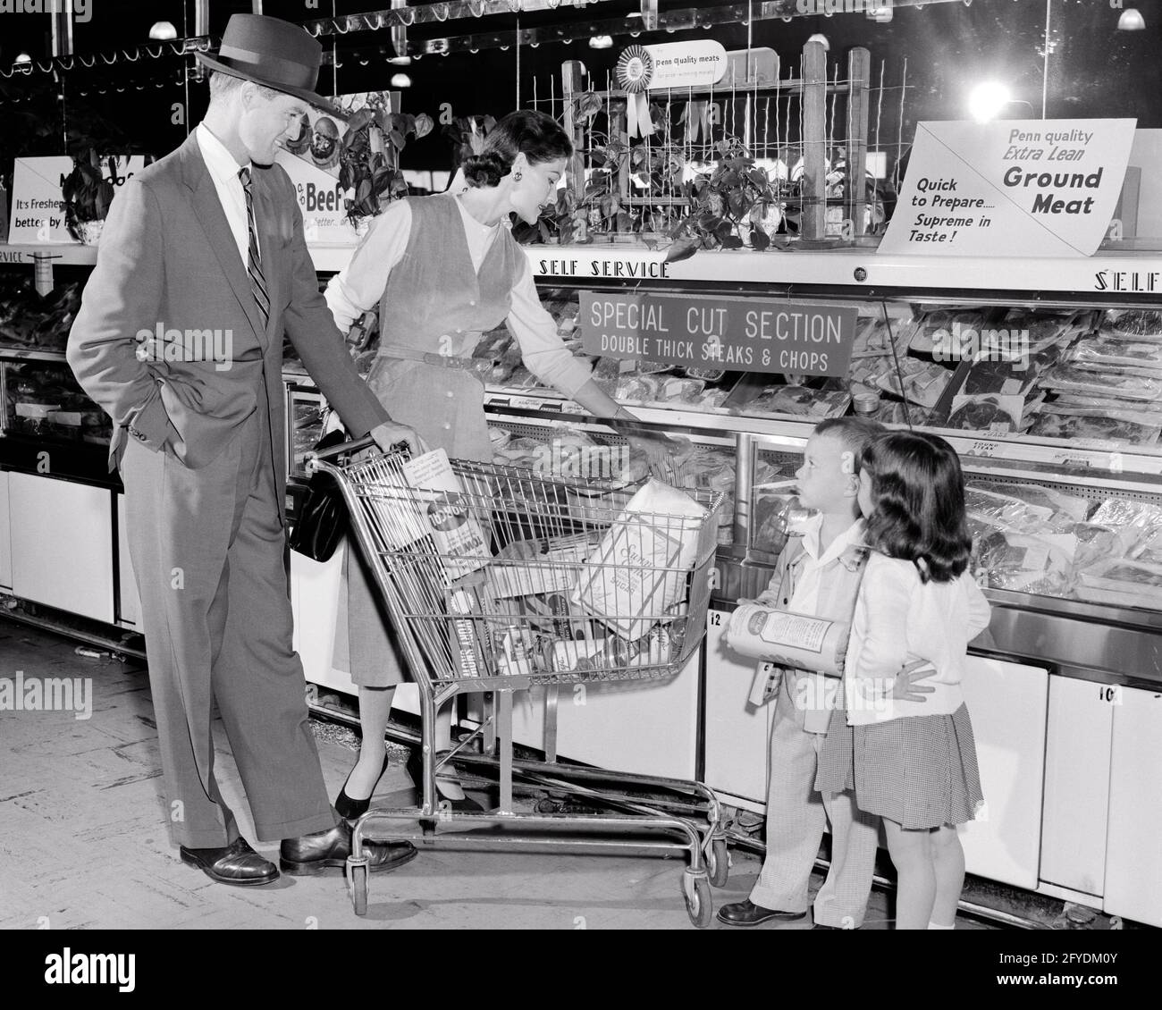 1950s FAMILY OF FOUR SHOPPING IN GROCERY STORE WITH CART AT MEAT COUNTER MOTHER FATHER WITH SON AND DAUGHTER - s7018 HAR001 HARS NOSTALGIC PAIR 4 SUBURBAN URBAN CART GROCERIES MOTHERS OLD TIME NOSTALGIA BROTHER OLD FASHION SISTER 1 JUVENILE SONS FAMILIES LIFESTYLE FEMALES MARRIED BROTHERS SPOUSE HUSBANDS COPY SPACE FULL-LENGTH LADIES DAUGHTERS PERSONS MALES MEAT SIBLINGS SISTERS FATHERS B&W PARTNER SHOPPER SHOPPERS SUIT AND TIE AND CHOICE DADS SIBLING STYLISH COOPERATION GROWTH JUVENILES MID-ADULT MID-ADULT MAN MID-ADULT WOMAN MOMS TOGETHERNESS WIVES BLACK AND WHITE CAUCASIAN ETHNICITY HAR001 Stock Photo