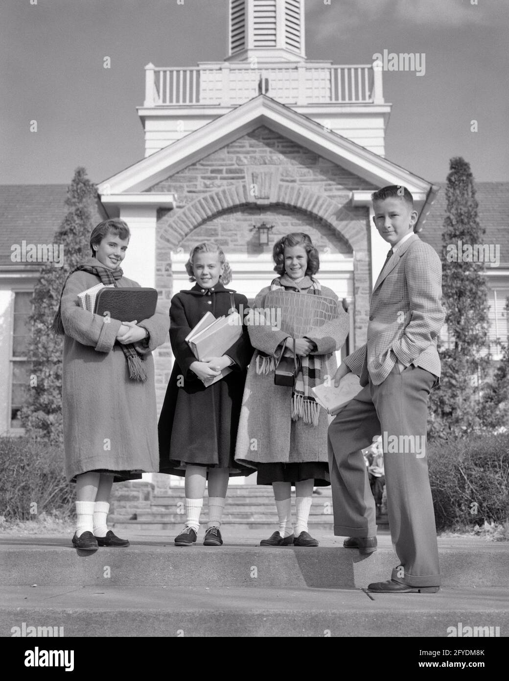 1950s 4 TEENAGERS STANDING IN FRONT OF SCHOOL BUILDING WEARING COATS CARRYING BOOKS 3 GIRLS AND 1 BOY ALL LOOKING AT CAMERA - s9726 HAR001 HARS COMMUNITY SUBURBAN OLD TIME BUSY NOSTALGIA OLD FASHION 1 JUVENILE STYLE TEAMWORK PLEASED JOY LIFESTYLE CELEBRATION FEMALES COATS COPY SPACE FRIENDSHIP FULL-LENGTH PERSONS MALES TEENAGE GIRL TEENAGE BOY CONFIDENCE B&W EYE CONTACT SCHOOLS SUIT AND TIE HAPPINESS CHEERFUL AND KNOWLEDGE PRIDE OPPORTUNITY HIGH SCHOOL SMILES HIGH SCHOOLS CONNECTION JOYFUL STYLISH TEENAGED JUNIOR COOPERATION GROWTH JUVENILES TOGETHERNESS BLACK AND WHITE CAUCASIAN ETHNICITY Stock Photo