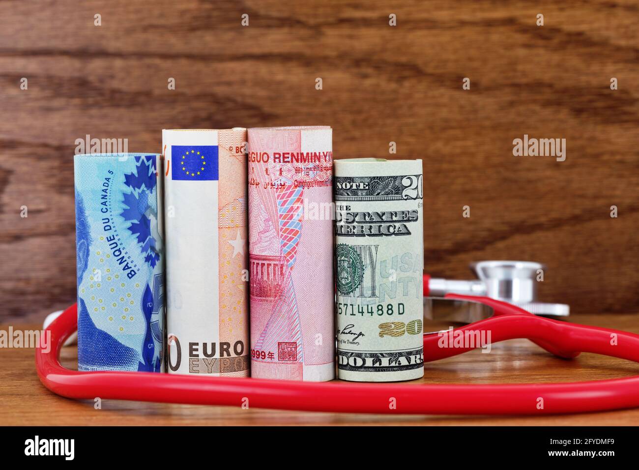 Scientific cooperation among nations in funding national and global health care seen in multiple currencies and red stethoscope on wood background Stock Photo
