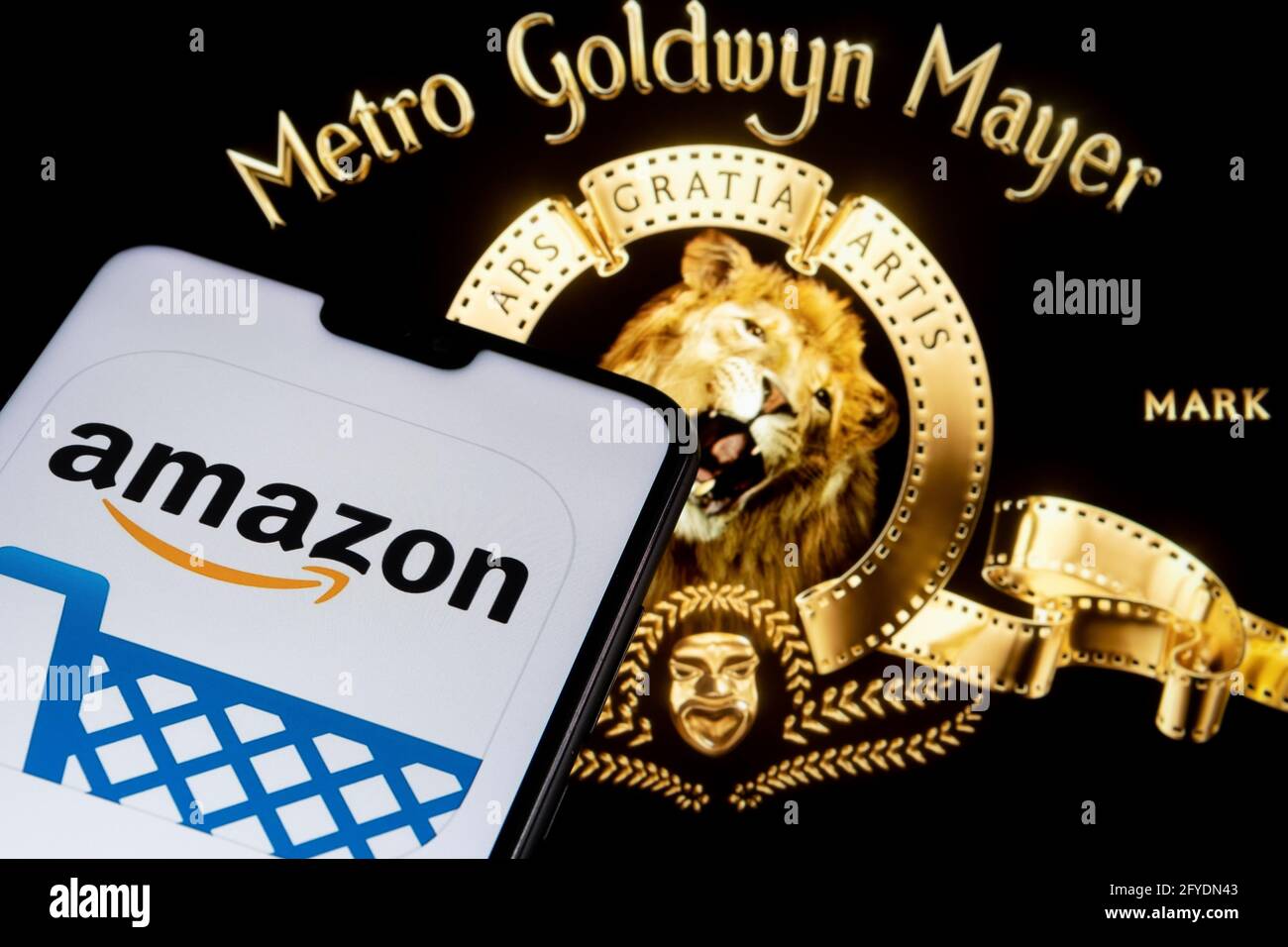 Amazon app logo seen on the smartphone and blurred Metro Goldwyn Mayer logo on the laptop. Stafford, United Kingdom, May 27, 2021. Stock Photo