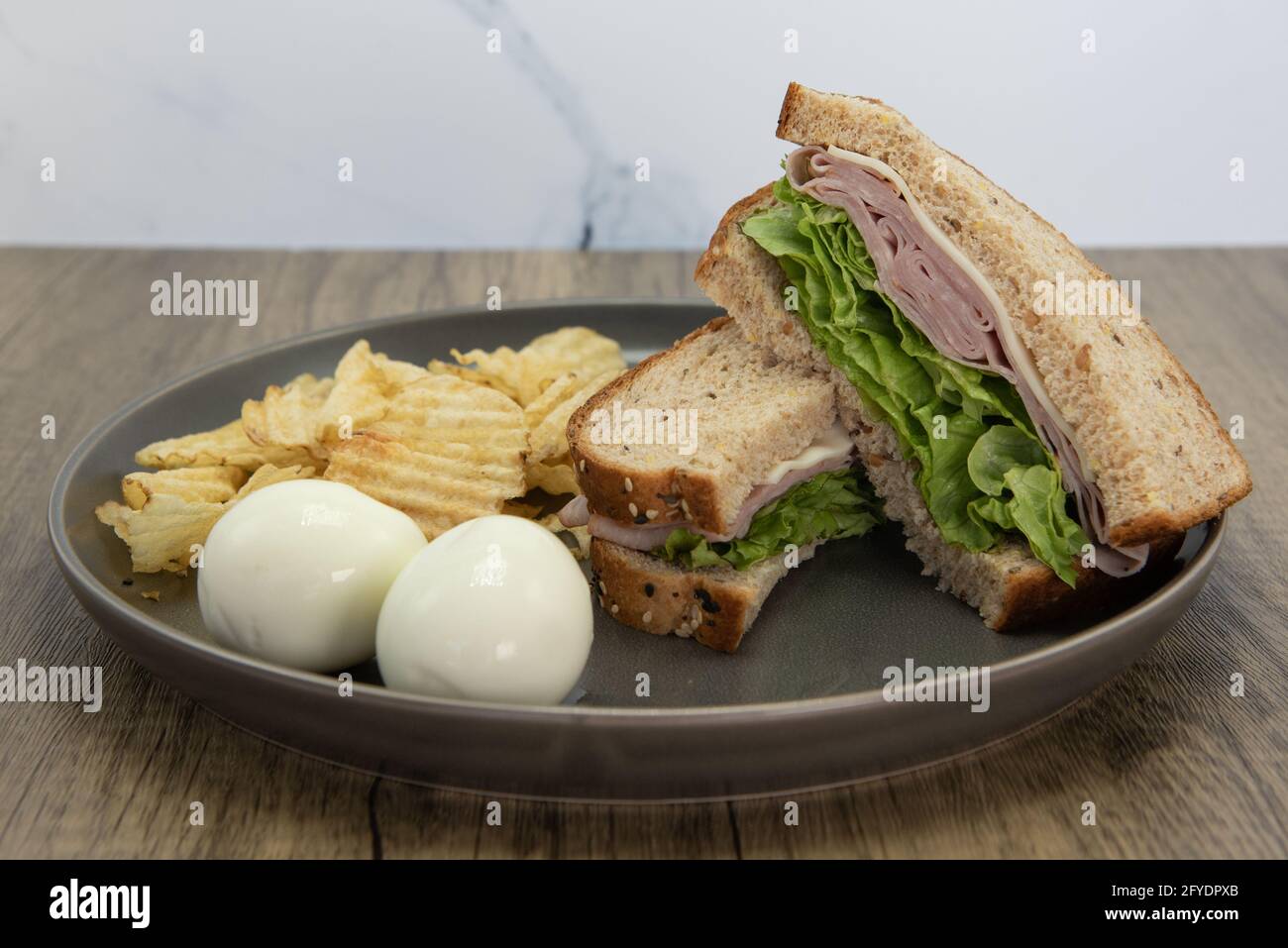 Appetizing ham and cheese sandwich with hardboiled eggs and chips is a perfect meal for a quick lunch break at work. Stock Photo