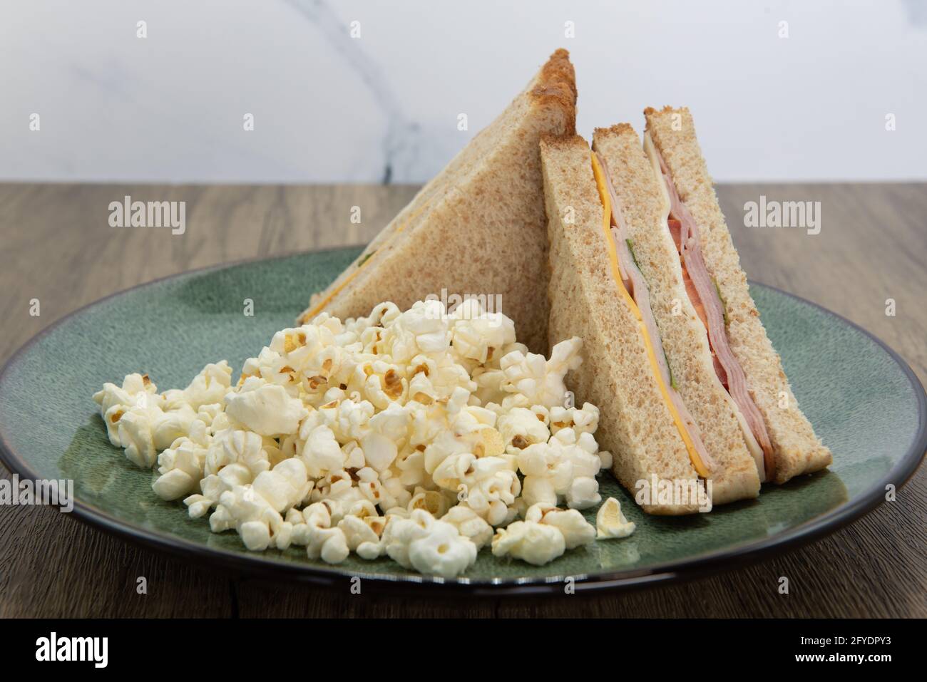 Double deck ham and cheese sandwich and popcorn is a perfect meal for a quick lunch break at work. Stock Photo