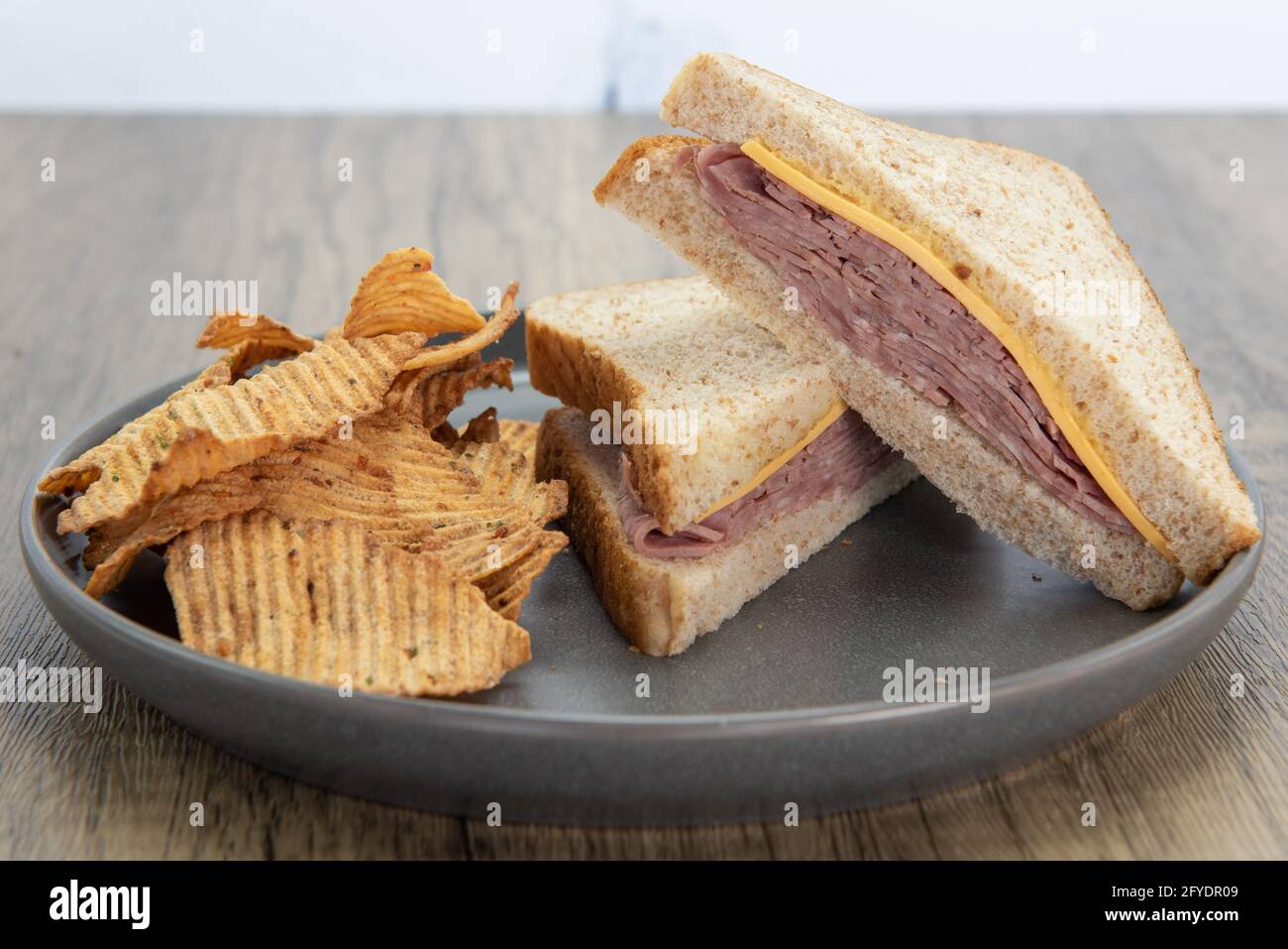 Appetizing triangle cut ham and cheese sandwich and chips is a perfect meal for a quick lunch break at work. Stock Photo