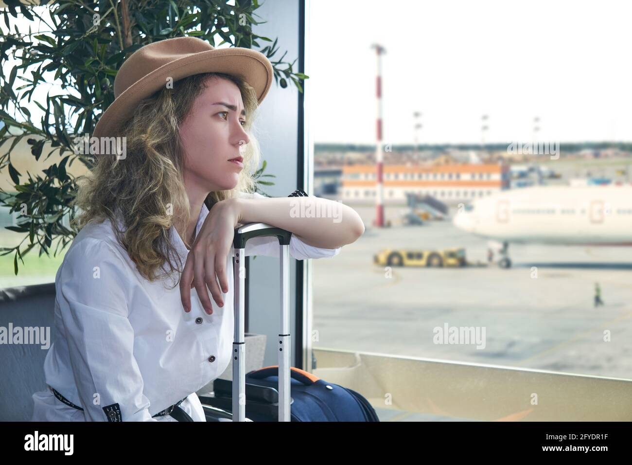 young woman traveler with suitcases sits in the waiting room of the airport and she is sad Stock Photo