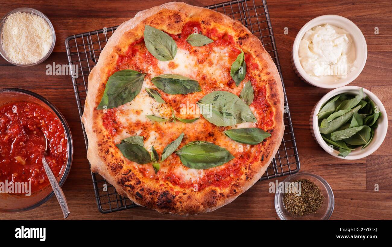 Overhead shot of freshly baked biga pizza with basil leaves and surrounded by several ingredients Stock Photo