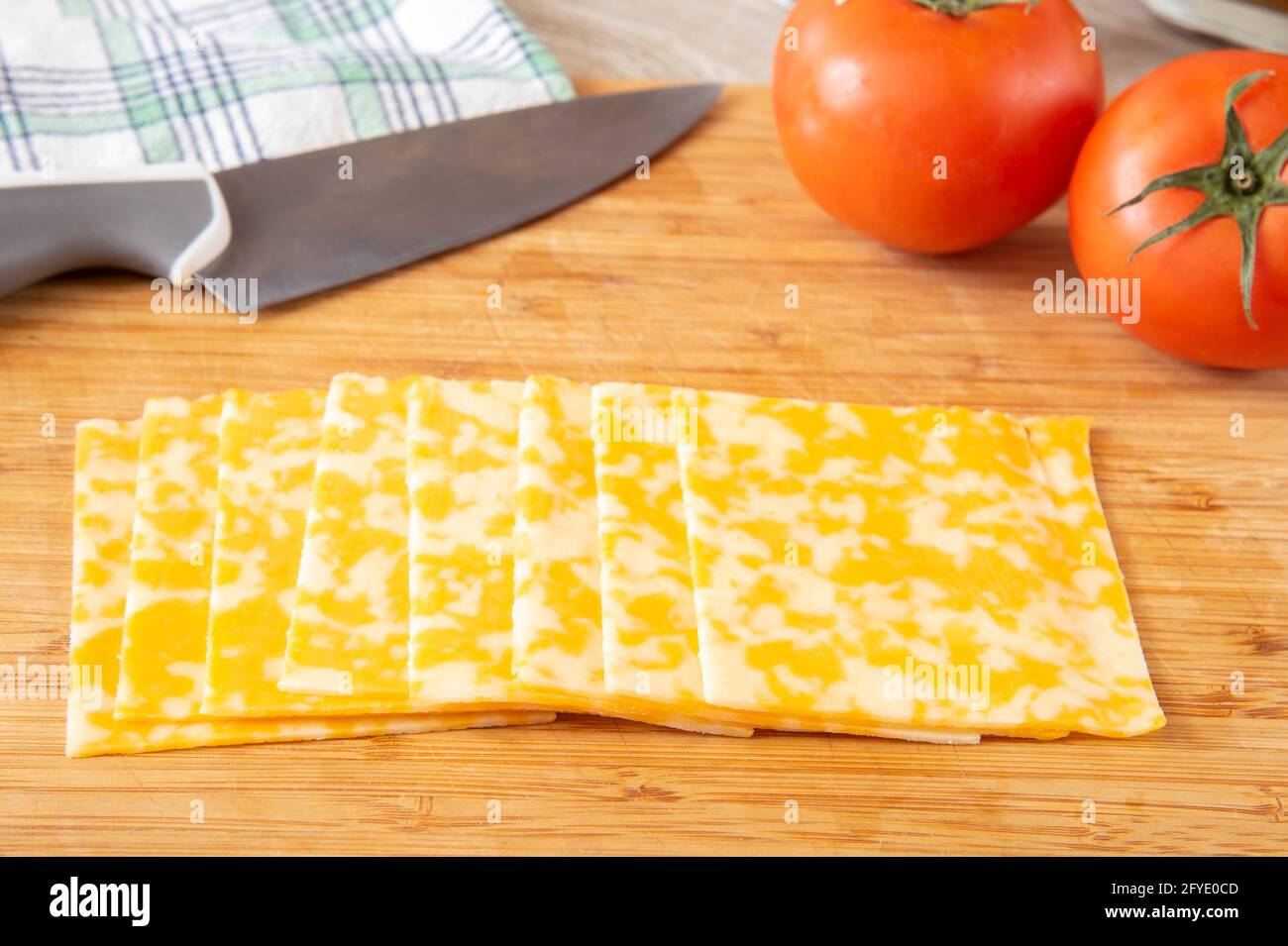 A stack of sliced colby cheese on a cutting board with fresh tomatos
