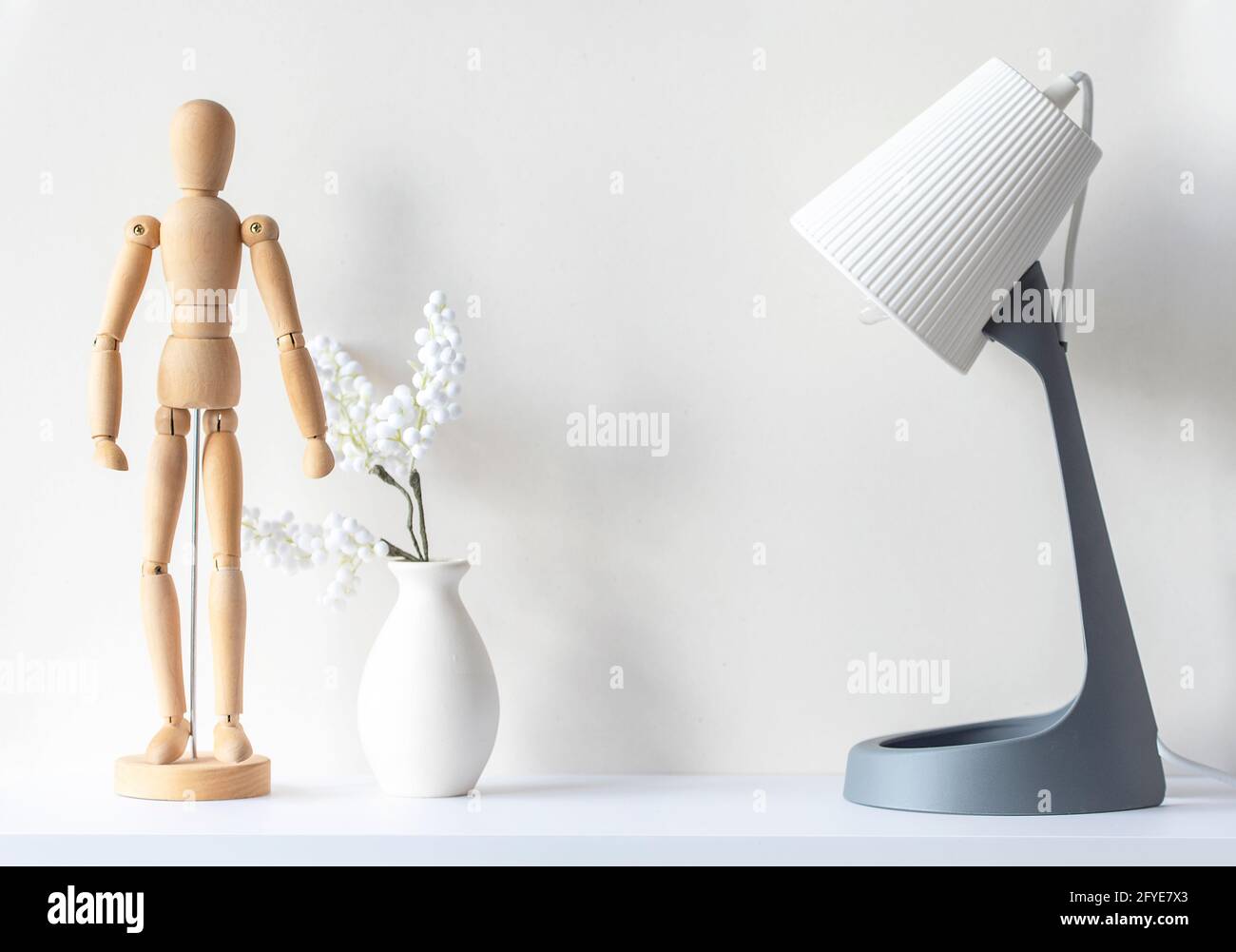 Interior of living room. Wooden mannequin, vase with decor plant, lamp on white wooden desk, mockup, minimal composition, space for text Stock Photo