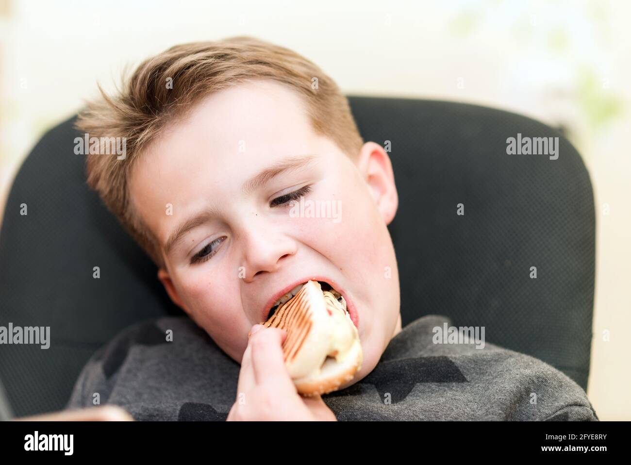 A Hungry boy eating a hot dog at home kid eats a hot-dog sandwich.Indoors shot.Closeup. Stock Photo
