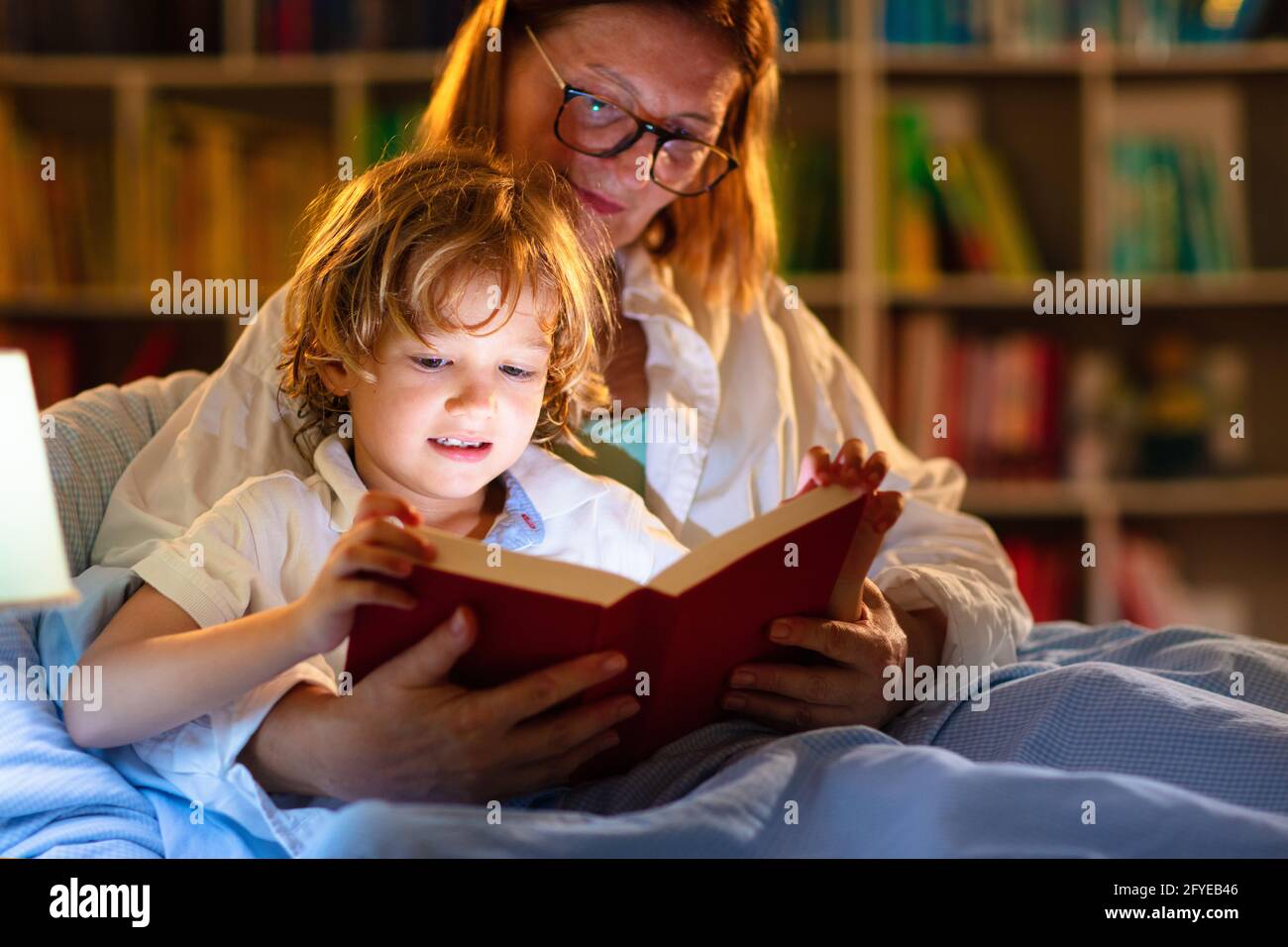 Child reading book in bed. Kids read at night. Little boy and mother