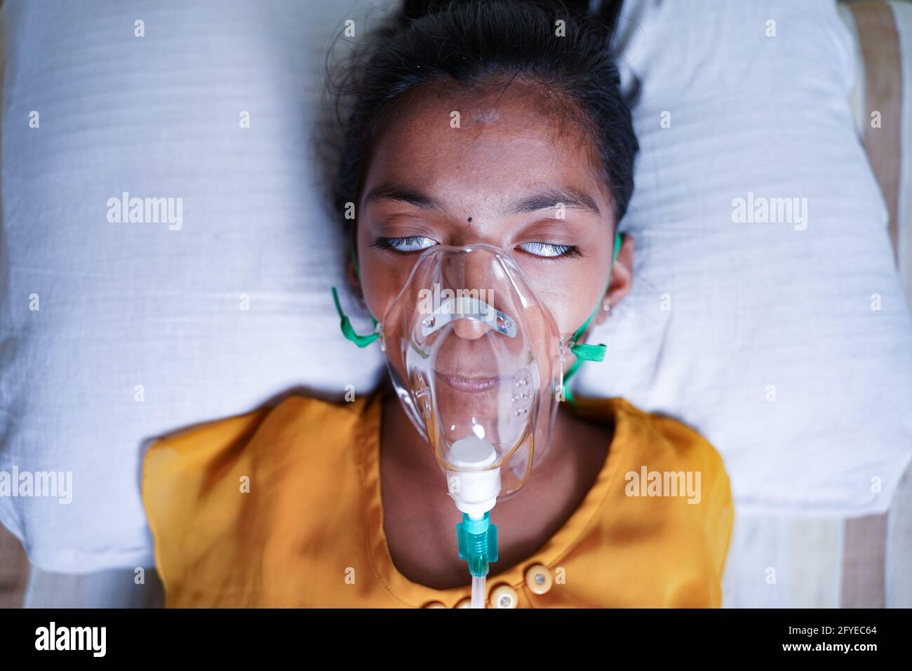 Close up top view of young kid breathing on ventilator oxygen mask due to coronavirus covid-19 breathlessness or dyspnea - concept of children Stock Photo