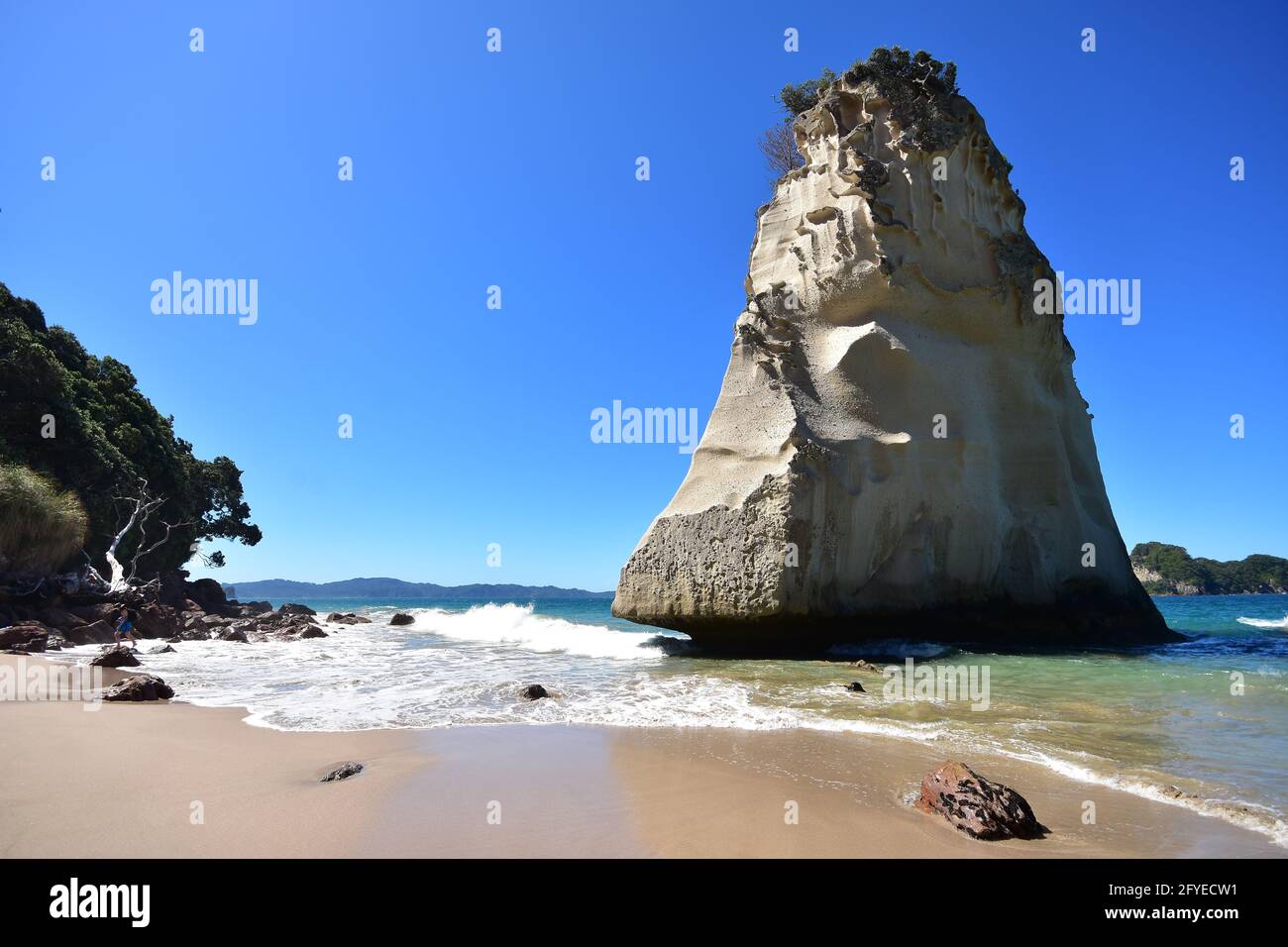 Massive block of rock in shallow water on sandy beach washed by oceanic surf. Stock Photo