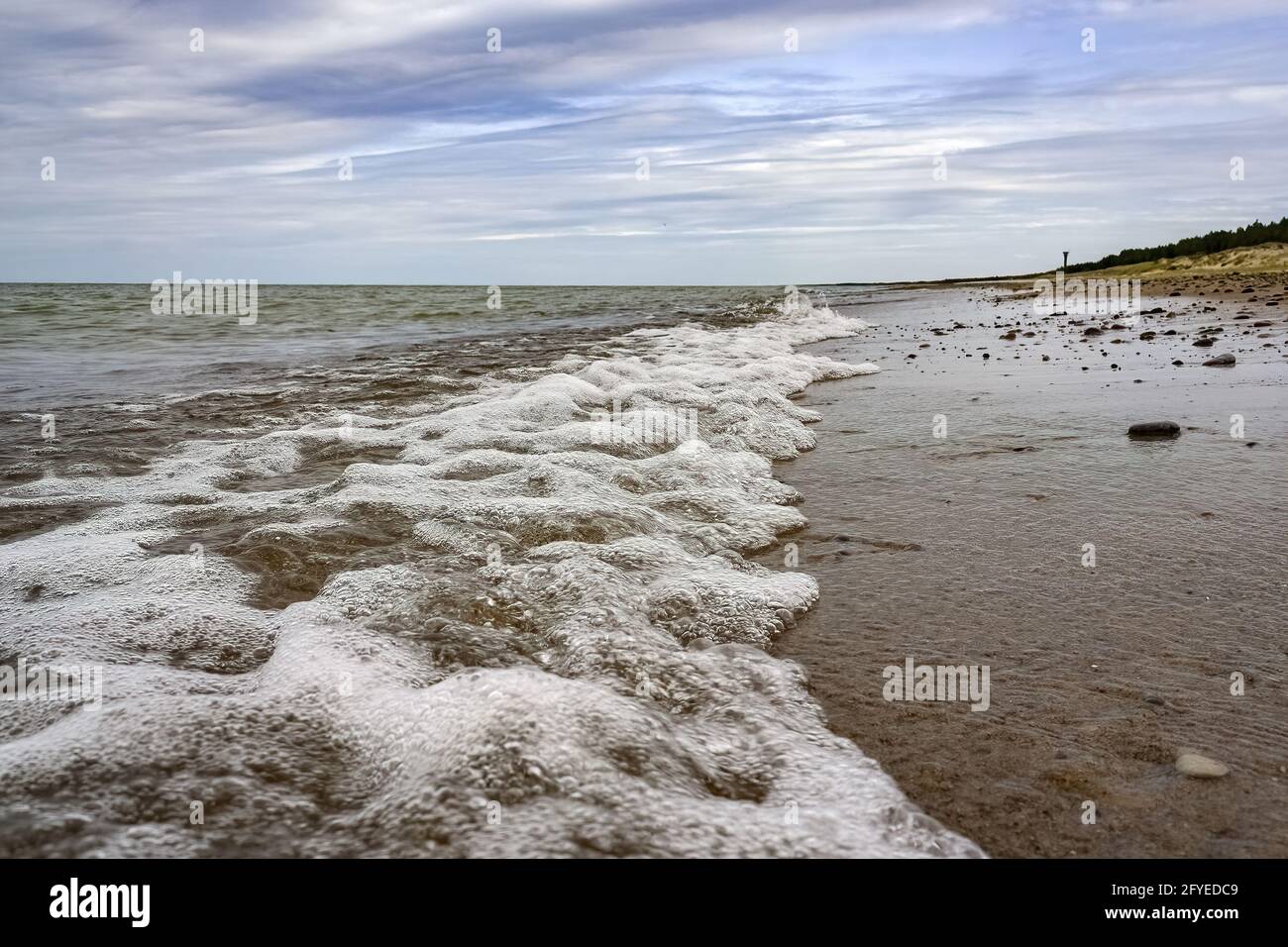 Sandy beach and wavy sea under cloudy sky Stock Photo - Alamy