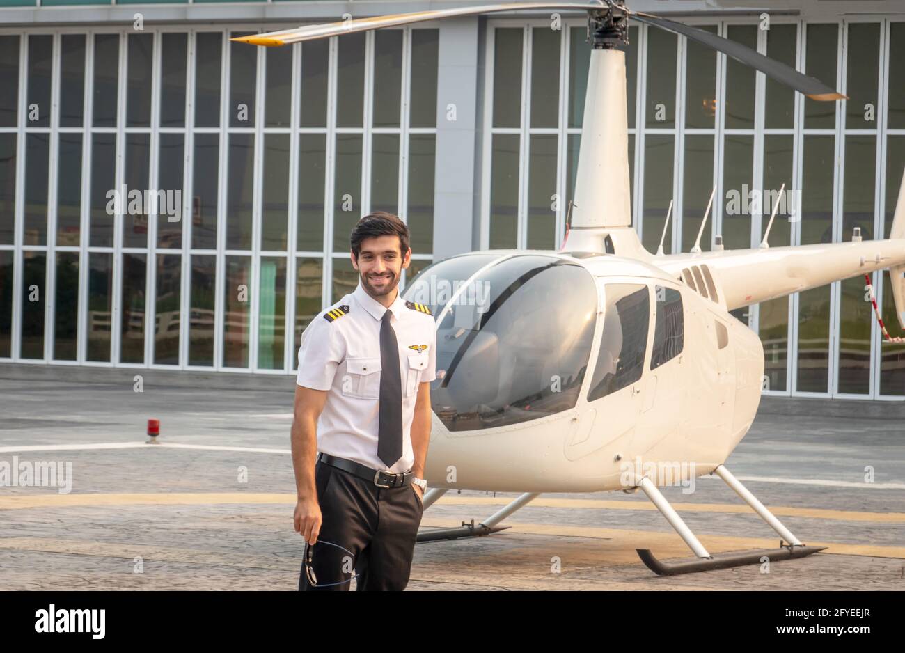 Commercial man pilot in technician suit standing in front of helicopter after check and maintenance engine Stock Photo