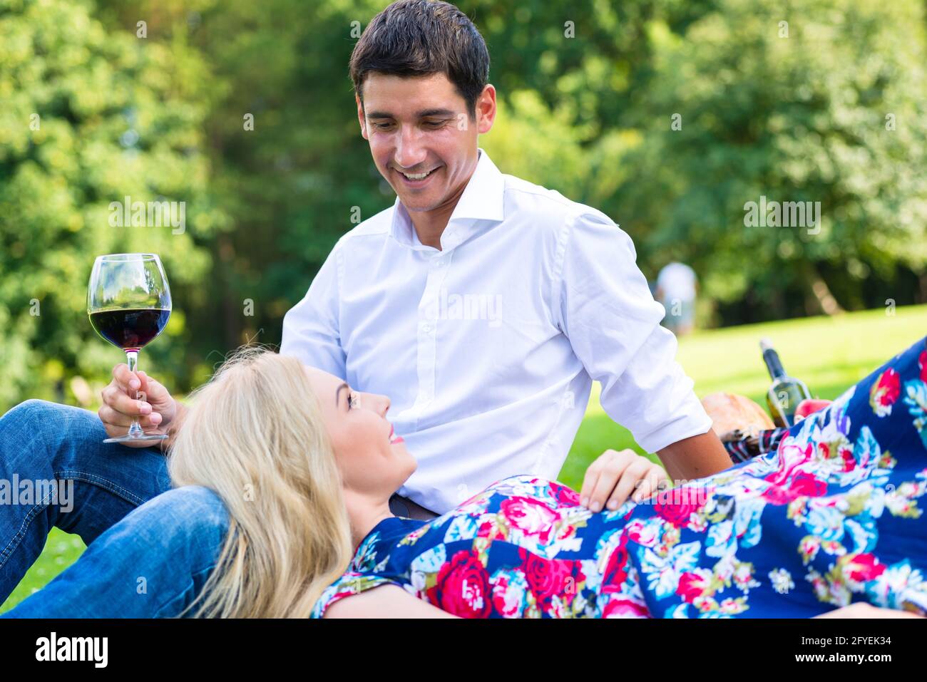 Couple drinking red wine on grass of park at picnic Stock Photo - Alamy