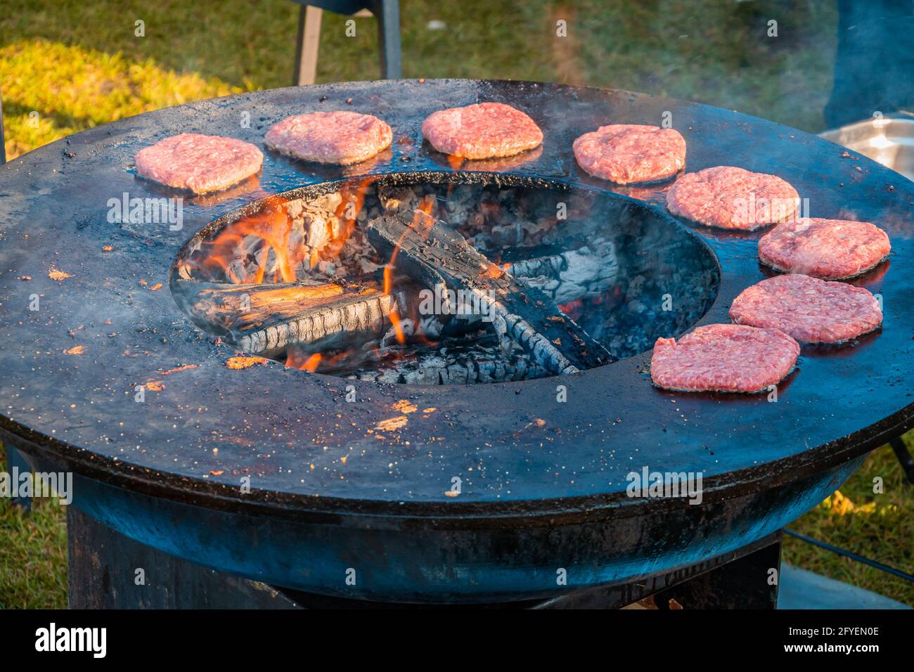 On the a large round wood-burning is roasting patties for burgers. Barbecue festival in the park. Street fast food Stock Photo - Alamy
