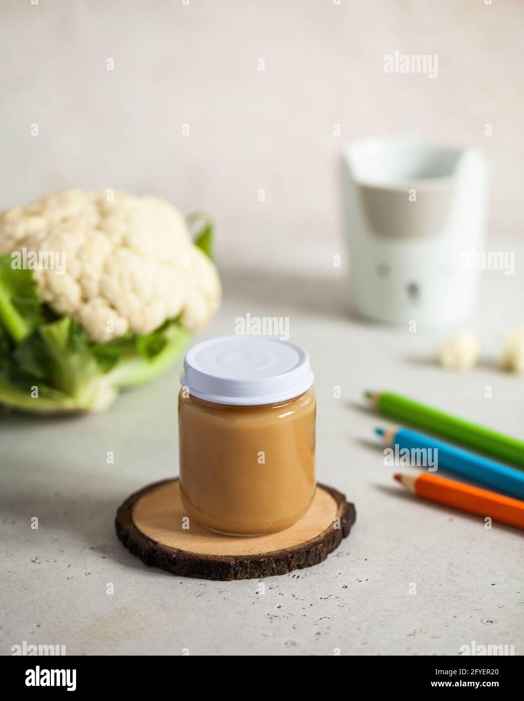 Closed glass jar with baby food cauliflower puree with fresh cauliflower and colored pencils. The concept of baby food Stock Photo