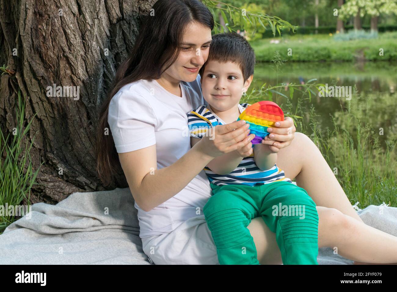 Mom and baby boy 4 years old play with a colored trendy toy Pop it in the park in nature. Antistress sensitive toy or reusable bubble wrap. Trend of 2 Stock Photo