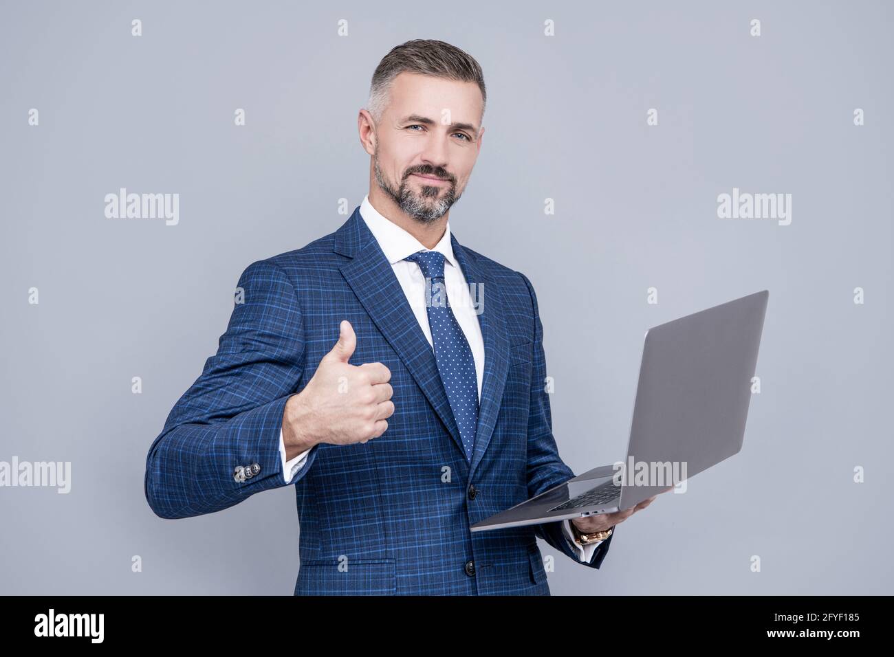 confident businessman man in businesslike suit hold computer show thumb up, success Stock Photo