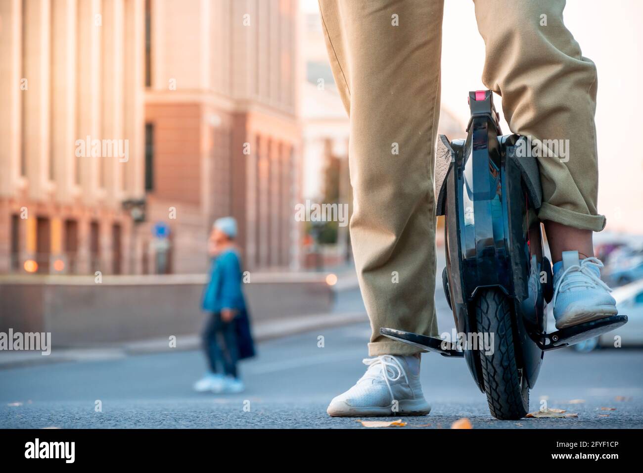 The legs of a young woman ready to ride an electric unicycle, abbreviated EUC, against the background of an evening or morning urban landscape. An unr Stock Photo