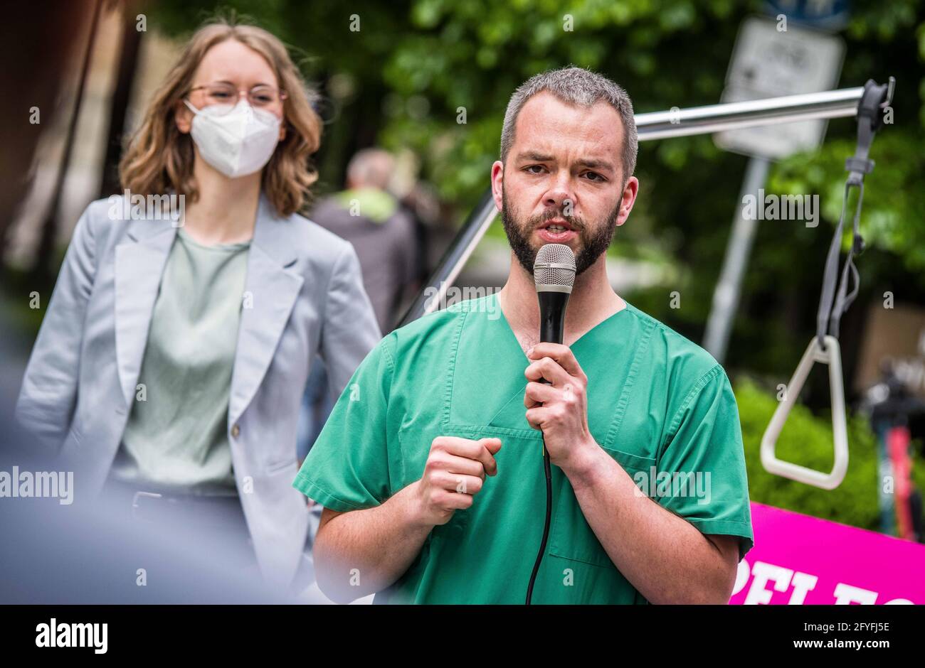 Munich, Bavaria, Germany. 28th May, 2021. ANDREAS KAHL of the Bavarian Greens wearing his hospital scrubs Kahl works in an Intensive Care Unit in Murnau and detailed the poor treatment of the healthcare workers by the Bavarian government that promotes overwork, poorer care quality, and burnout syndrome. The Bavarian Greens (die Gruenen/Buendnis90) organized a protest action at the Bavarian Staatskanzlei (government building) in support of healthcare workers. During the Coronavirus crisis, the working conditions for this sector have come into greater focus and The Greens are pushing for better Stock Photo