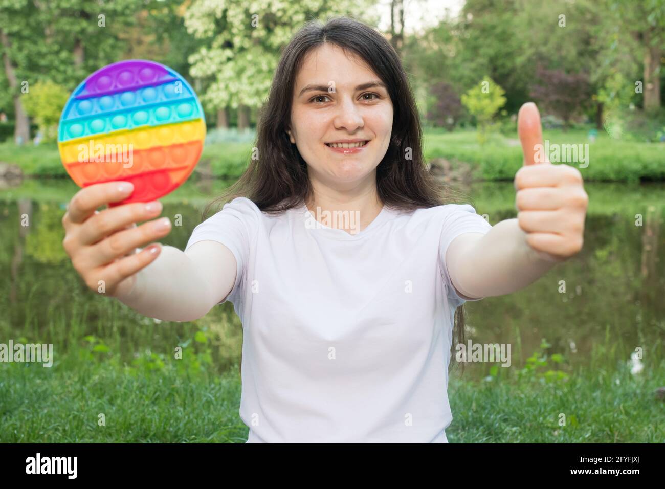 Brunette girl plays with a fashionable antistress toy pop it on nature. Trend 2021 is a sensitive reusable bubble wrap, a fun game against stress Stock Photo