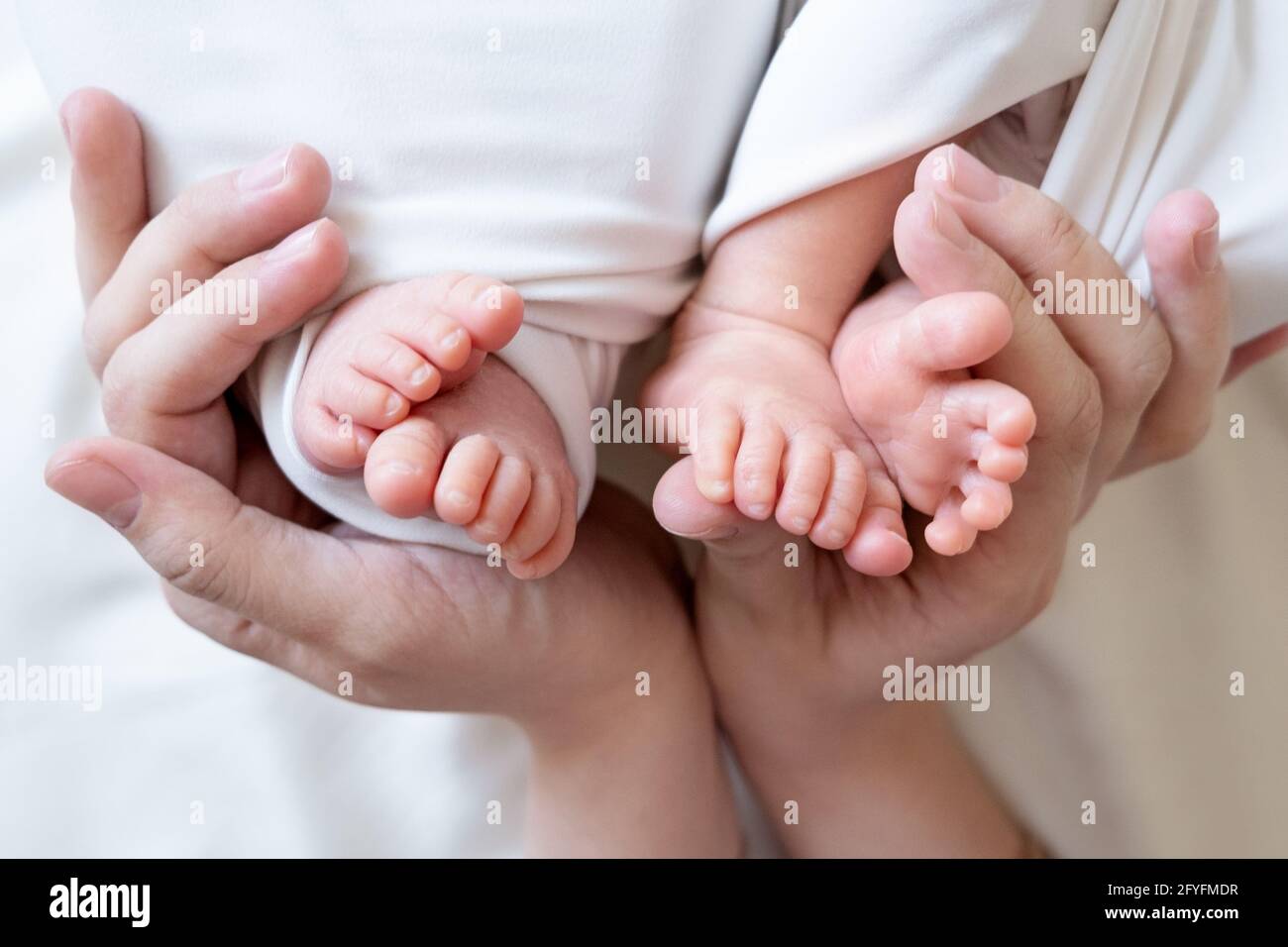 Mom and dad hands hold small legs of their two newborn twin babies