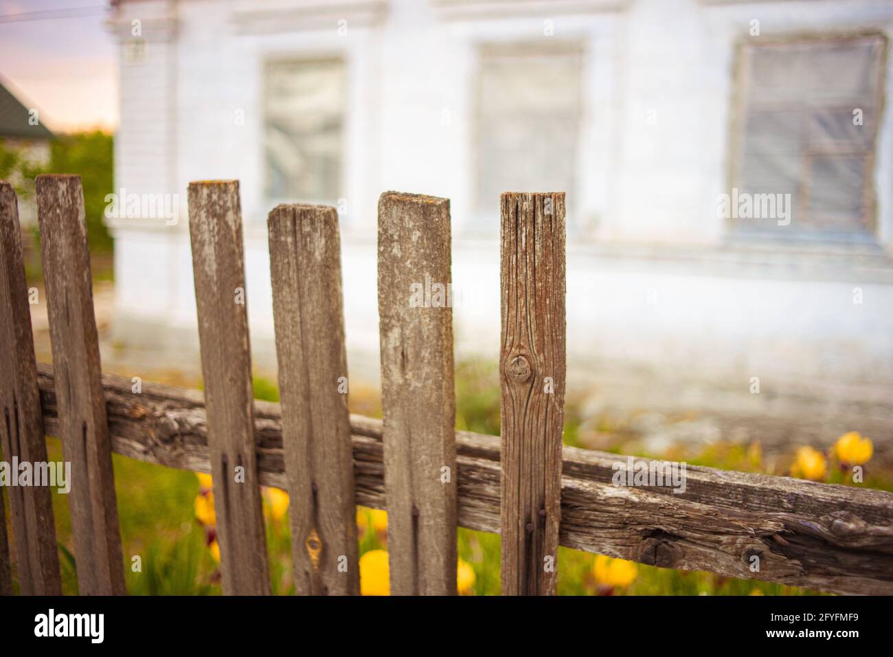 Old broken picket fence. White rural house in blurred background. Stock Photo