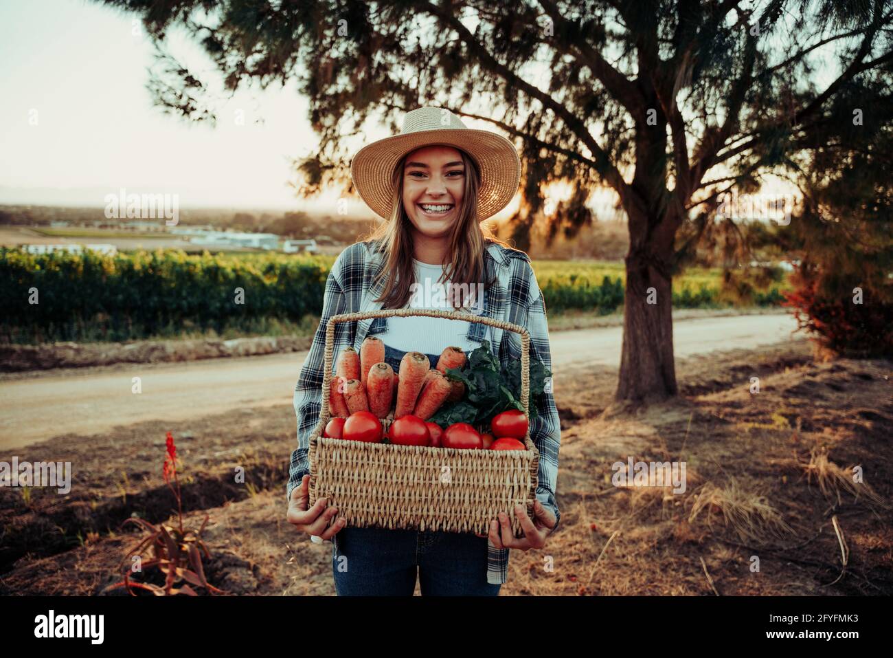 Caucasian female farmer giggling and smiling while holding fresh basket of vegetables Stock Photo