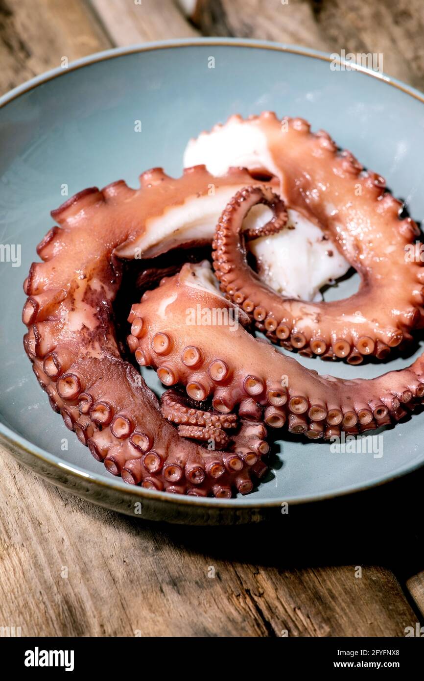 Coocked tentacles of octopus on blue ceramic plate over brown wooden background. Close up Stock Photo