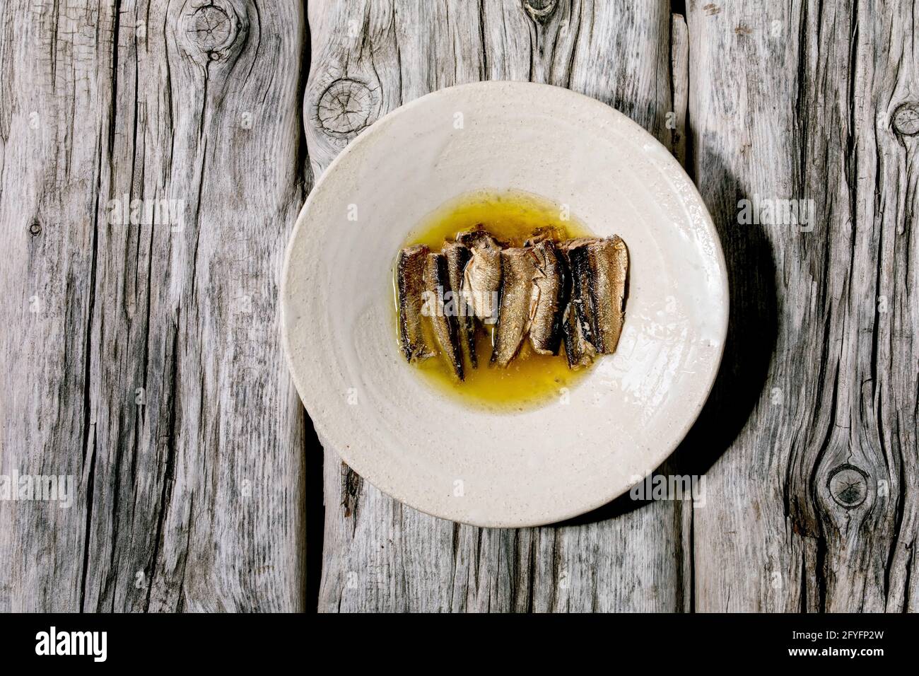 Smoked sardines in oil served in white ceramic plate over old grey wooden background. Top view