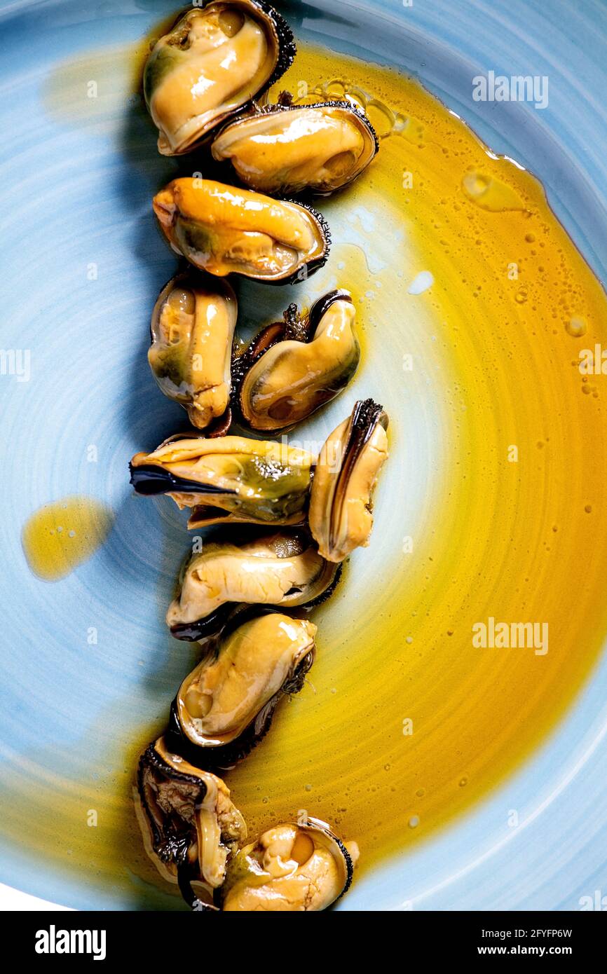 Smoked mussels in oil on blue ceramic plate. Top view, flat lay. Close up Stock Photo