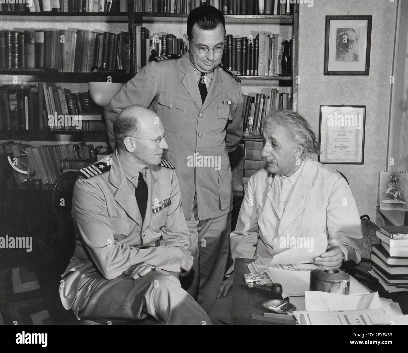 October 1943 Albert Einstein discusses documents with Naval officers in the study of his Princeton, New Jersey home. With him are Captain Geoffrey E. Sage, commanding officer of the United States Naval Training School in Princeton, and Lieutenant Commander Frederick L. Douthit of the United States Naval Reserves Stock Photo