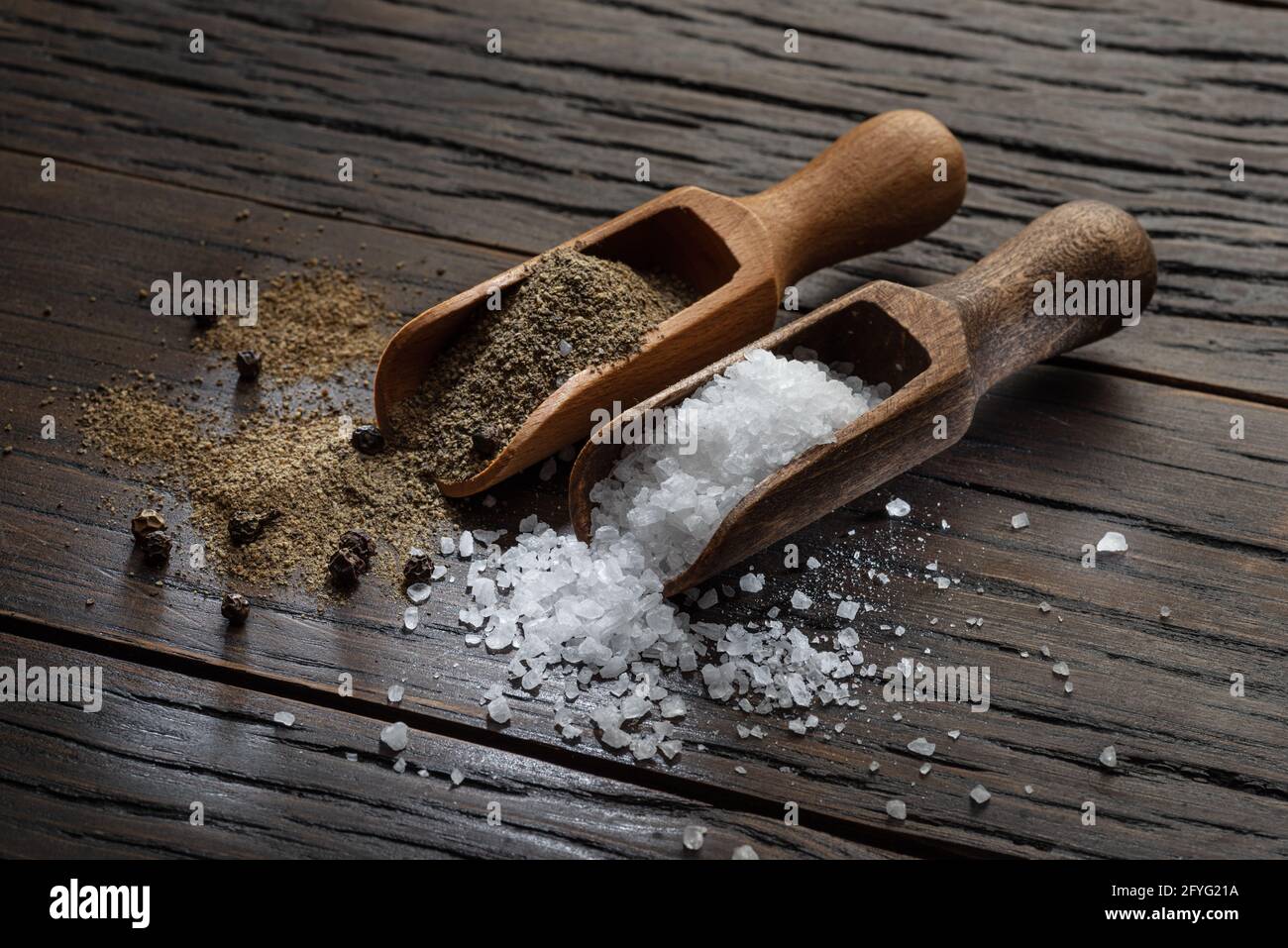 Sea salt and ground pepper in the wooden spoons on old wooden background. Two most popular ingredients that you put into food. Stock Photo