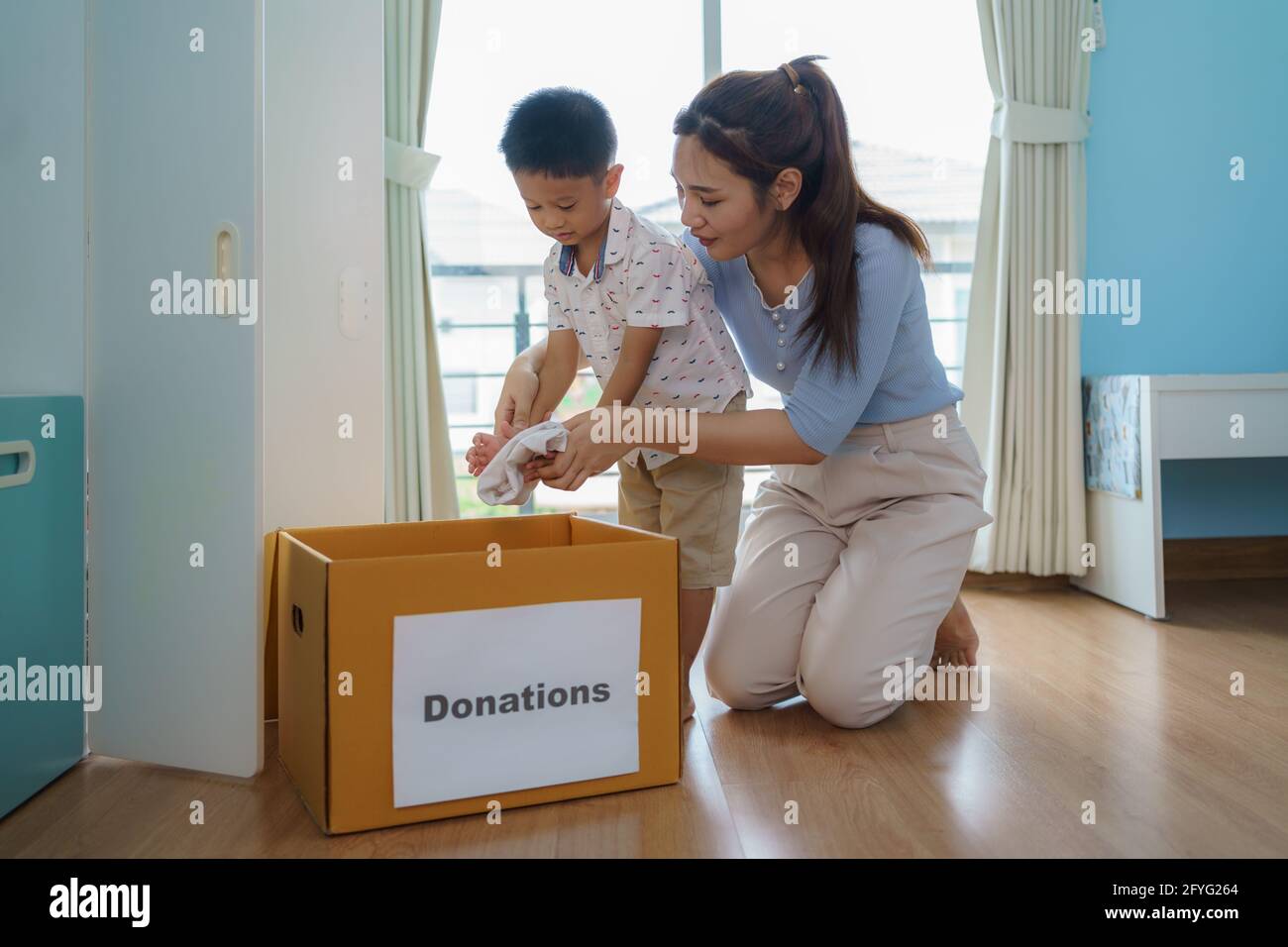 Asian mother and son are standing near closet of clothes in the dressing room carrying a box of clothes donated to take to the donation center. Stock Photo