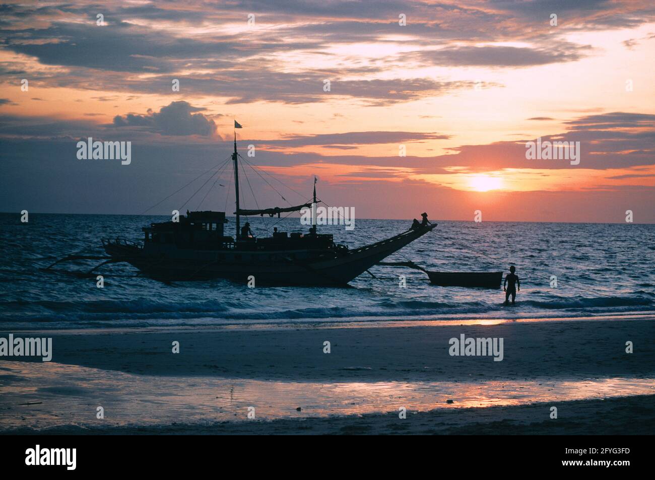 Philippines. Luzon region. Beach at sunset. Fishing boat and fishermen silhouetted. Stock Photo