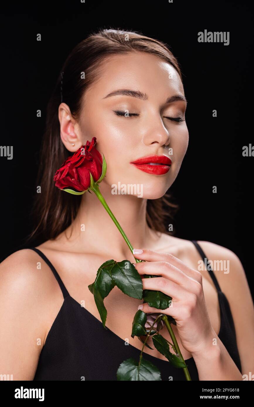 young woman with closed eyes holding red rose isolated on black Stock ...
