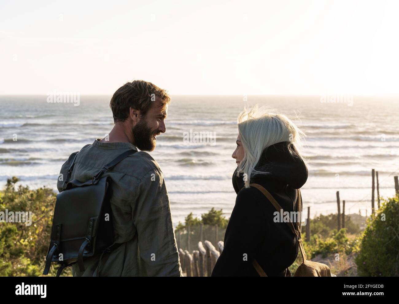 Romantic happy couple in love standing on wooden stairs on dunes at the wild beach in front of the sea - Boyfriend and girlfriend wearing vintage back Stock Photo