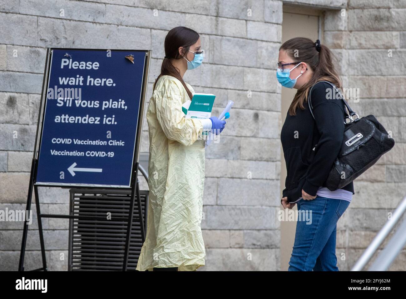 A person in PPE (Personal protective equipment) speaks with a person outside a COVID-19 vaccine clinic at Kingston general hospital (KGH) in Kingston, Stock Photo
